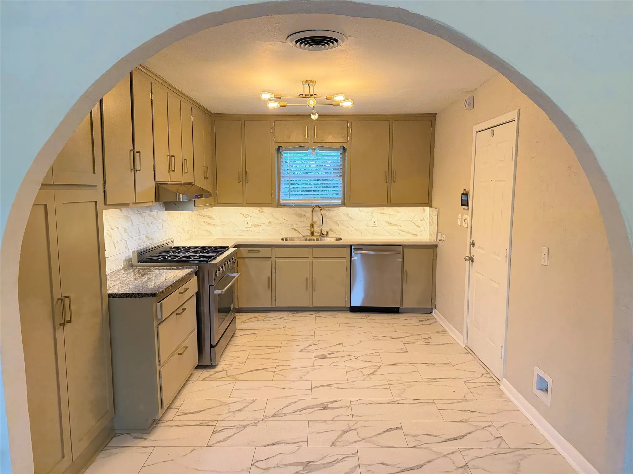 Kitchen featuring light-toned cabinetry, stainless steel appliances, a modern overhead light fixture, white and grey patterned flooring, and a corresponding backsplash