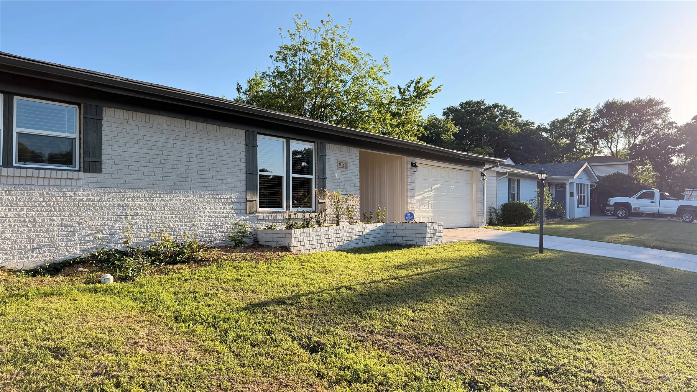 Light-colored brick exterior featuring dark window shutters, established front landscaping with a brick planter, and an attached two-car garage