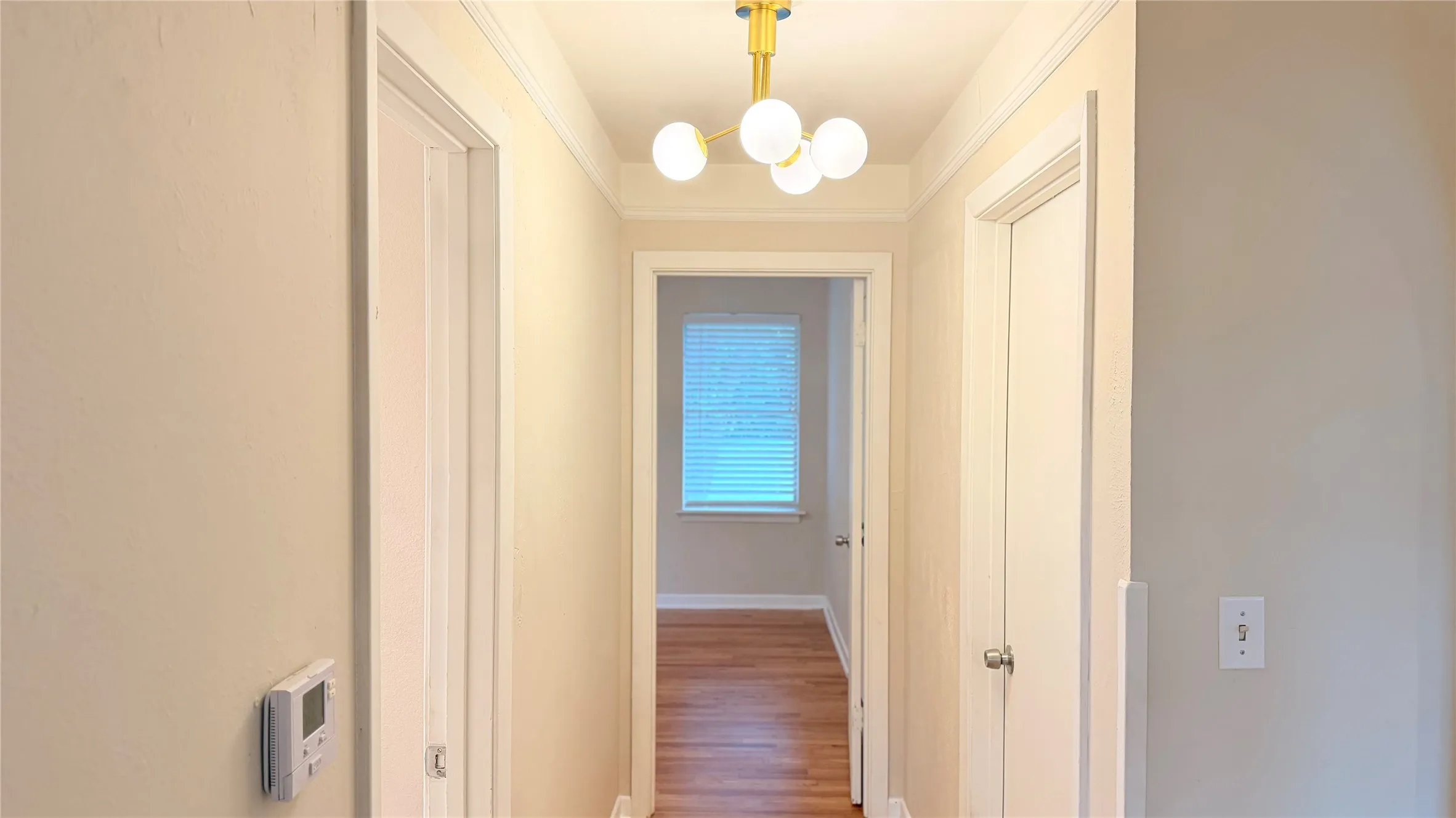 Hallway featuring a modern spherical chandelier, crown molding, and wood-finish flooring