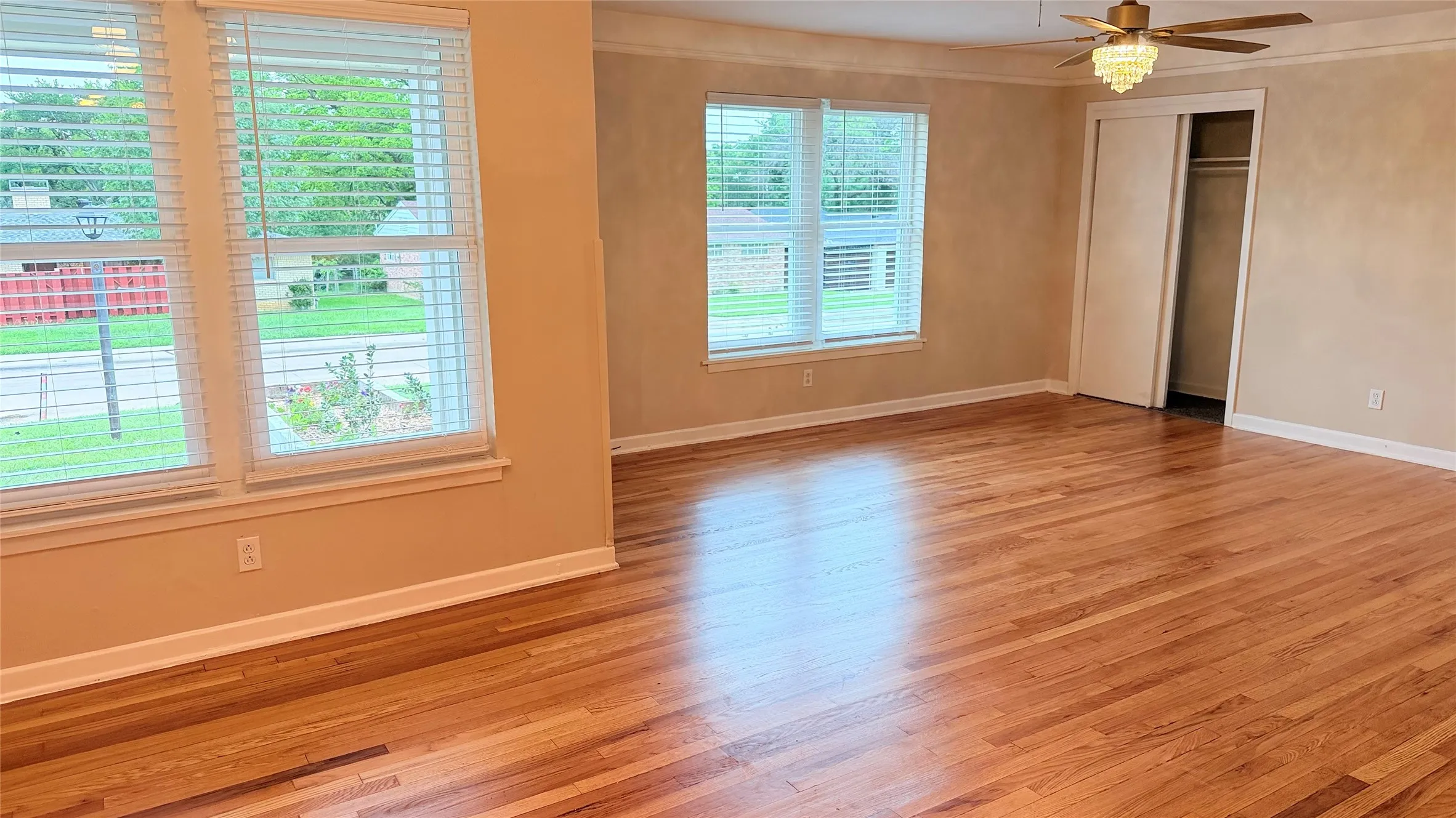 Spacious room featuring wood-finish flooring, multiple windows with blinds, a ceiling fan with light fixture, and a built-in closet with sliding doors