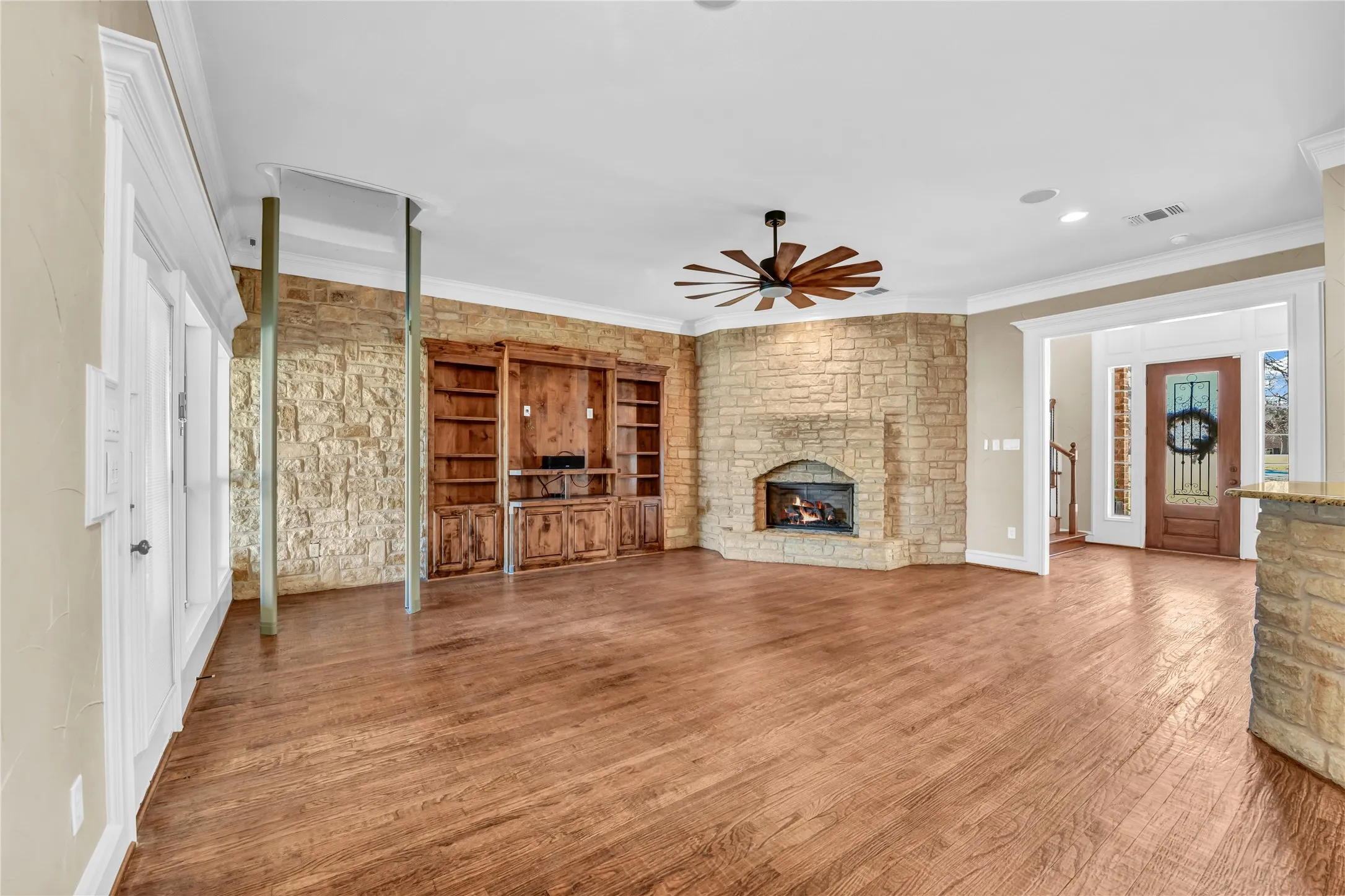  living room featuring a stone fireplace, wood finished floors, a ceiling fan, and ornamental molding