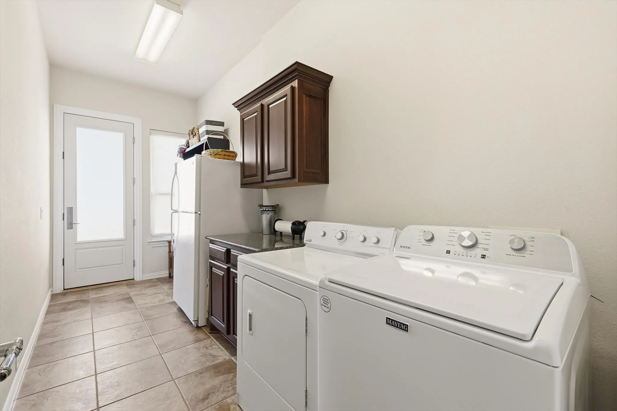 Laundry area with light tile patterned floors, built in cabinets and door leading to 3rd garage