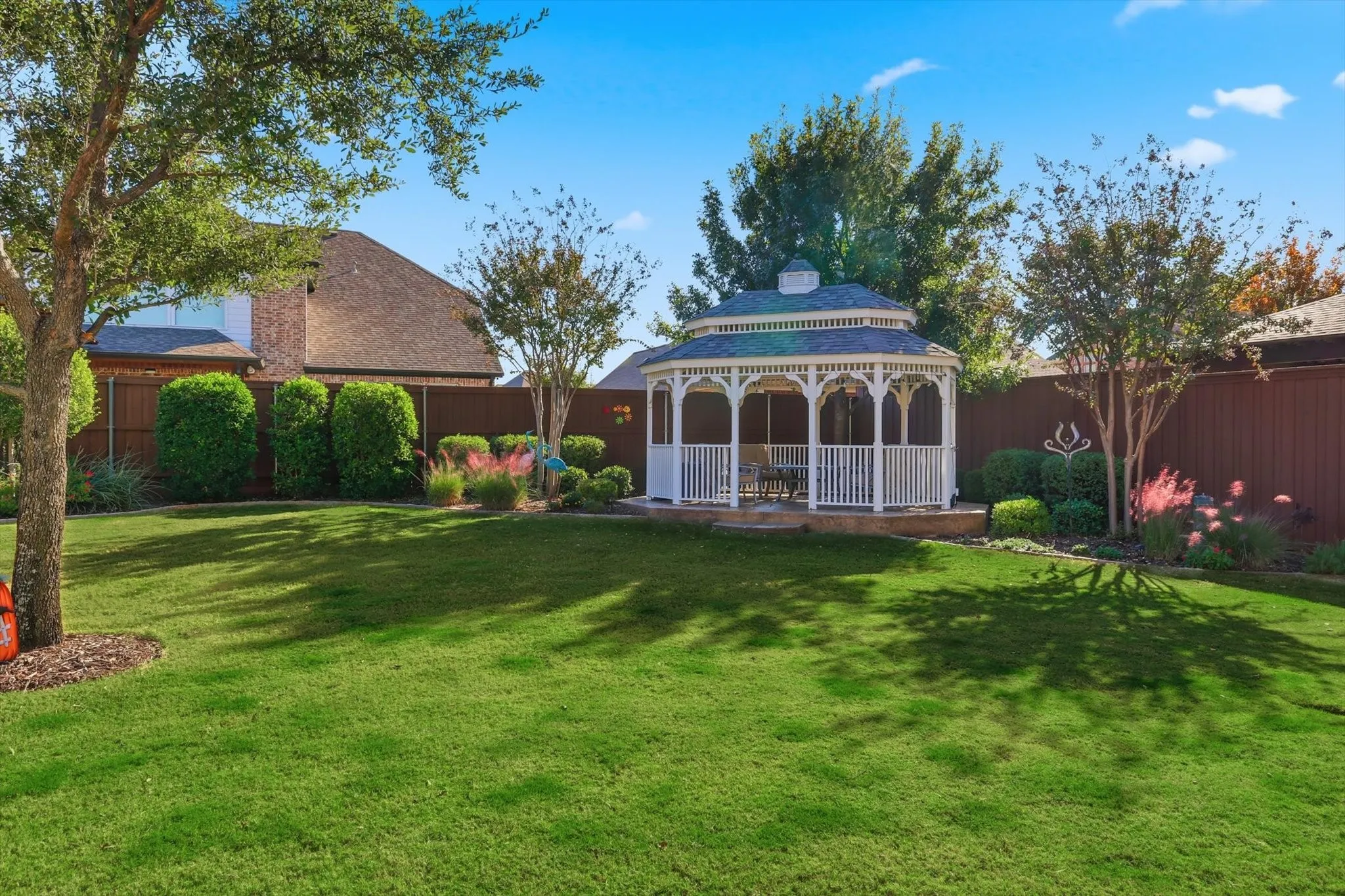 Large Fenced backyard featuring a gazebo and striking landscaping