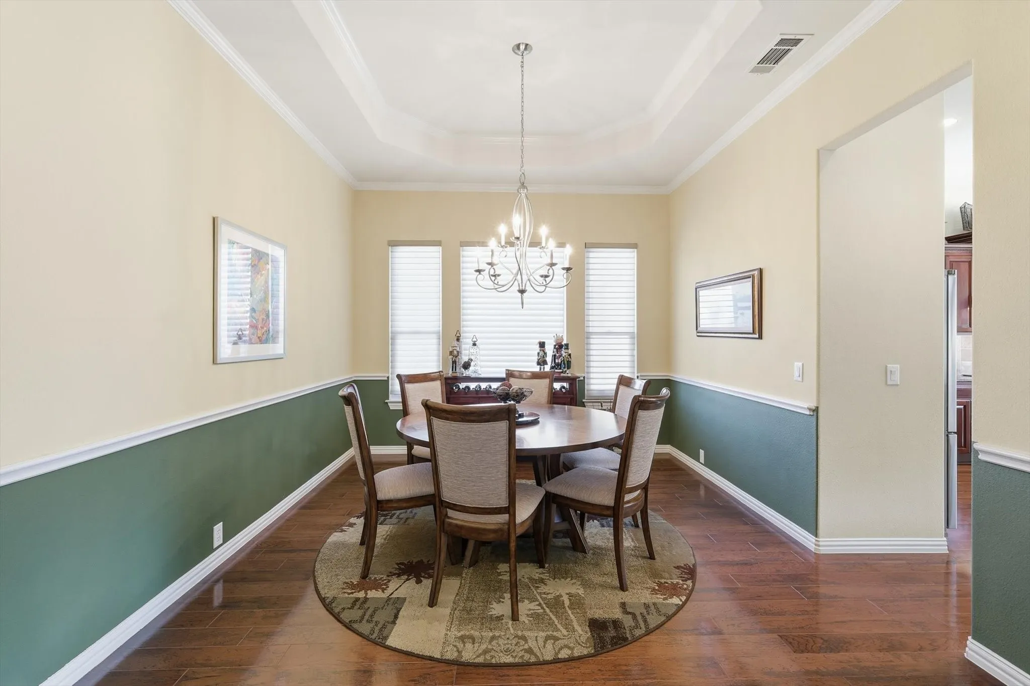 Dining space featuring a raised ceiling, dark wood-style flooring, a chandelier, and crown molding