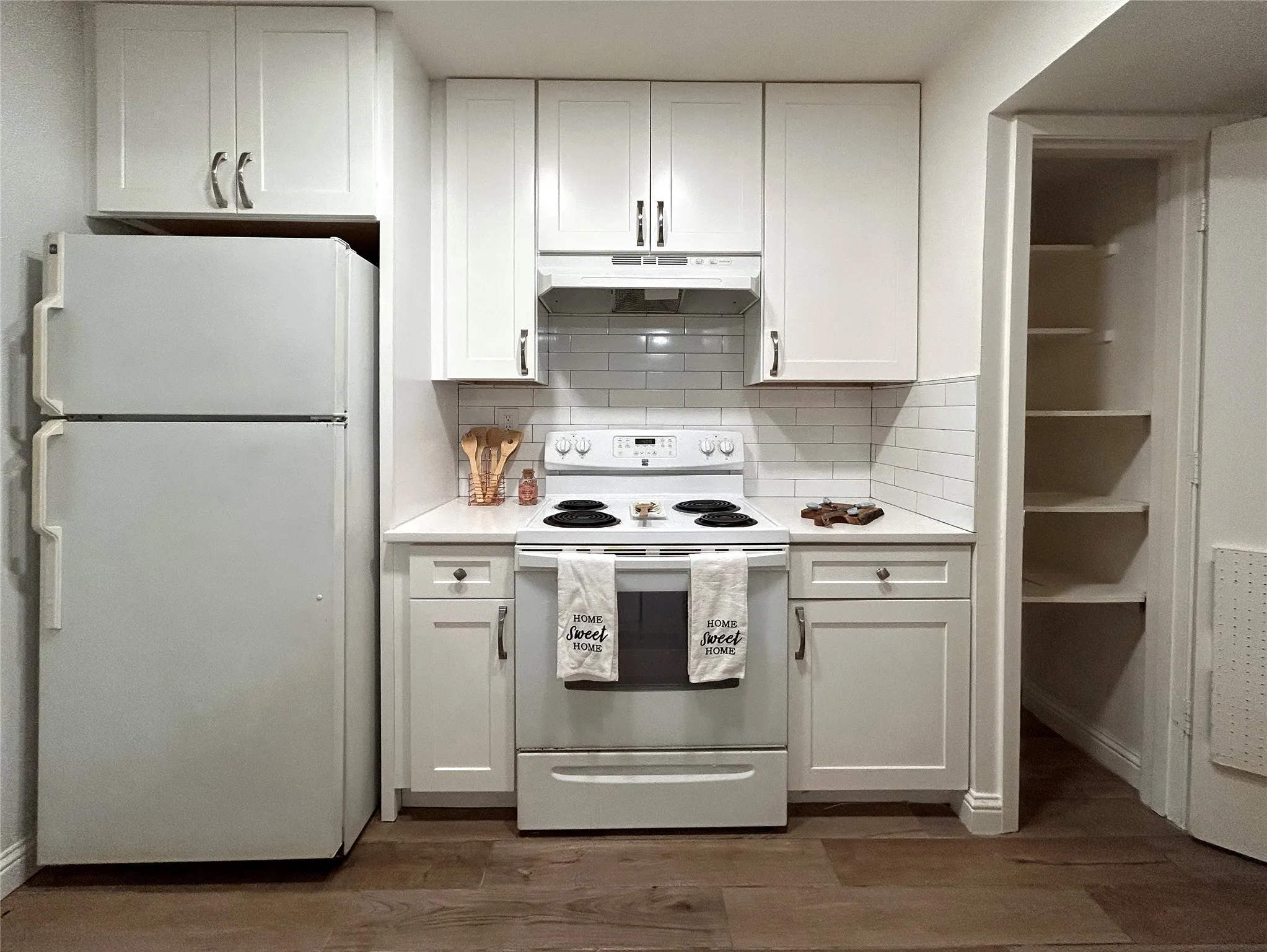 The kitchen has a convenient pantry, white appliances, white cabinetry, designer cabinets and subway tile backsplash.