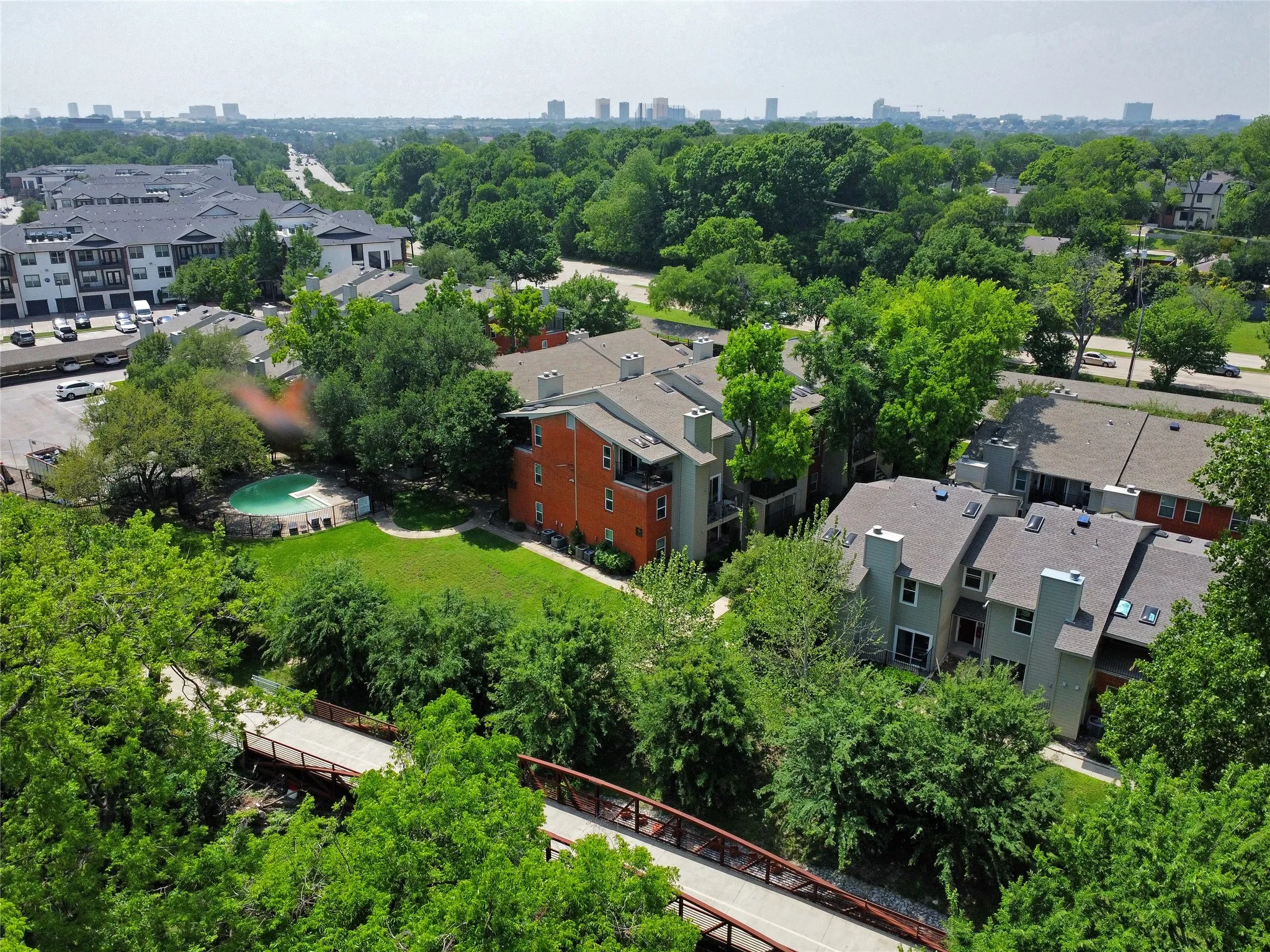 A butterfly zips high above the community pool. A drone view shows the back of building from above the creek toward Lake Highlands Trail bridge and Dallas skyscrapers in the distance.