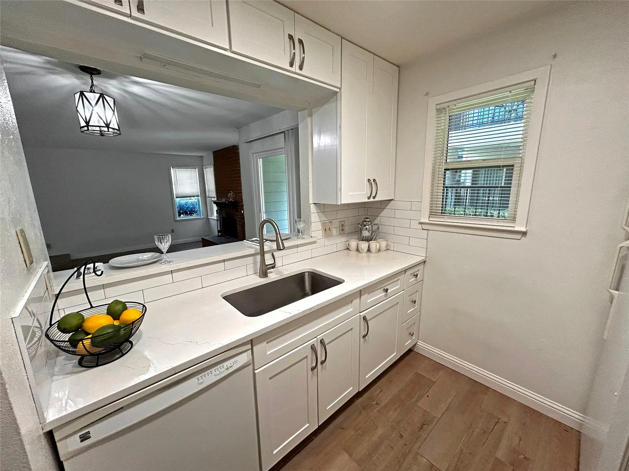 The kitchen has a window, breakfast bar, stainless steel sink, white dishwasher, white cabinetry, designer cabinets and subway tile backsplash.