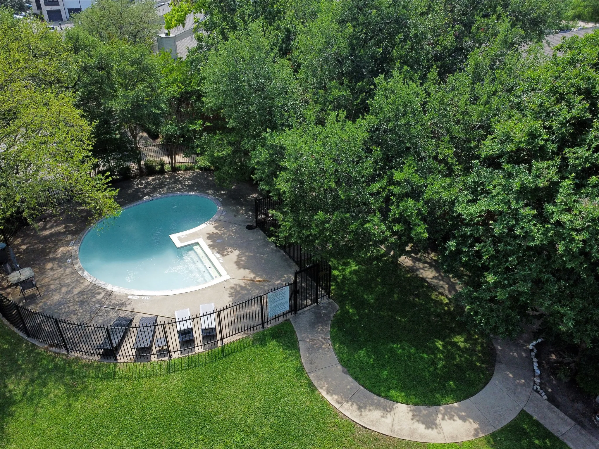 The freeform community swimming pool has integrated steps, surrounded by a concrete deck and a black metal fence. It is located at the back of the building.