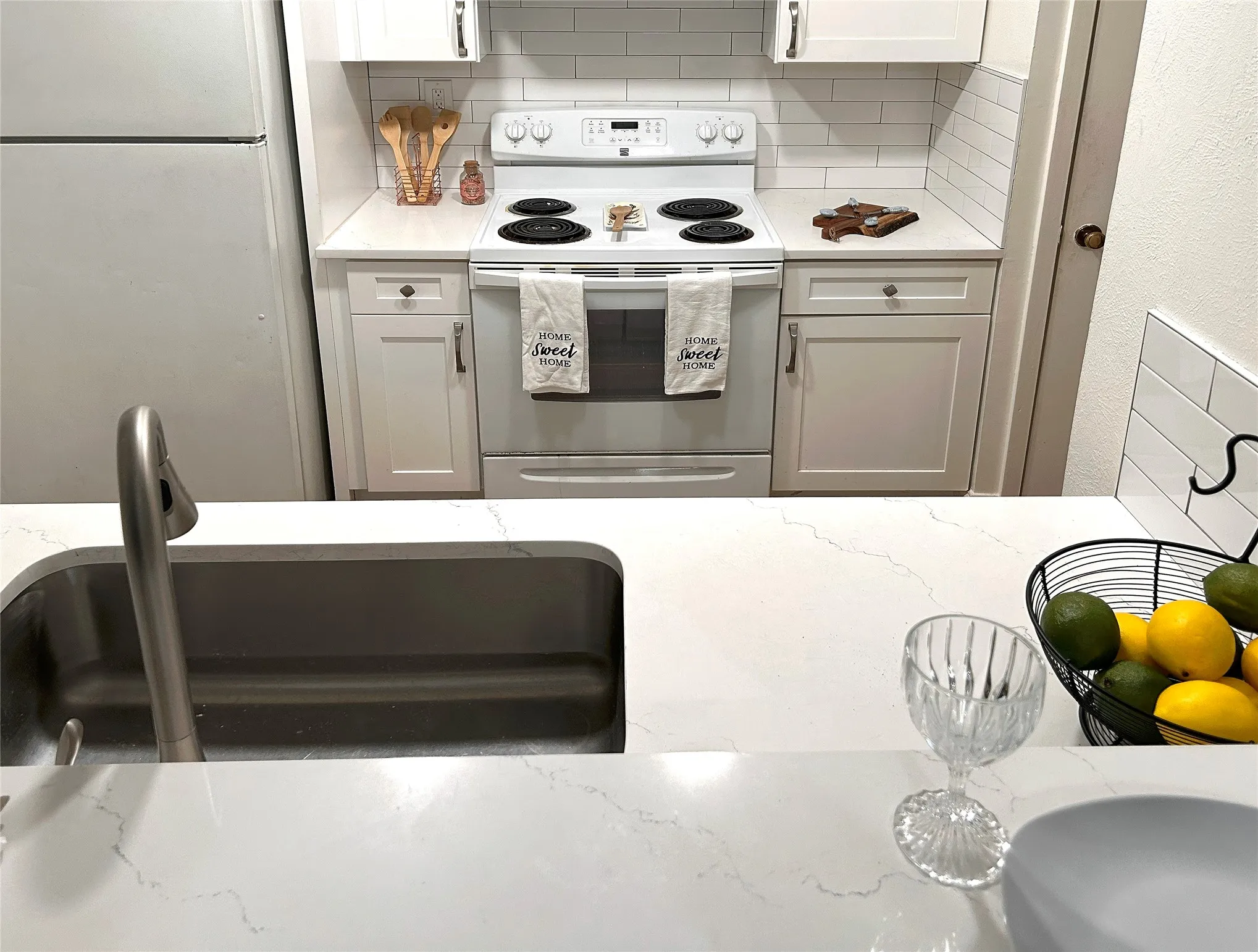 The kitchen has a sink, white appliances, white cabinetry, designer cabinets and subway tile backsplash.