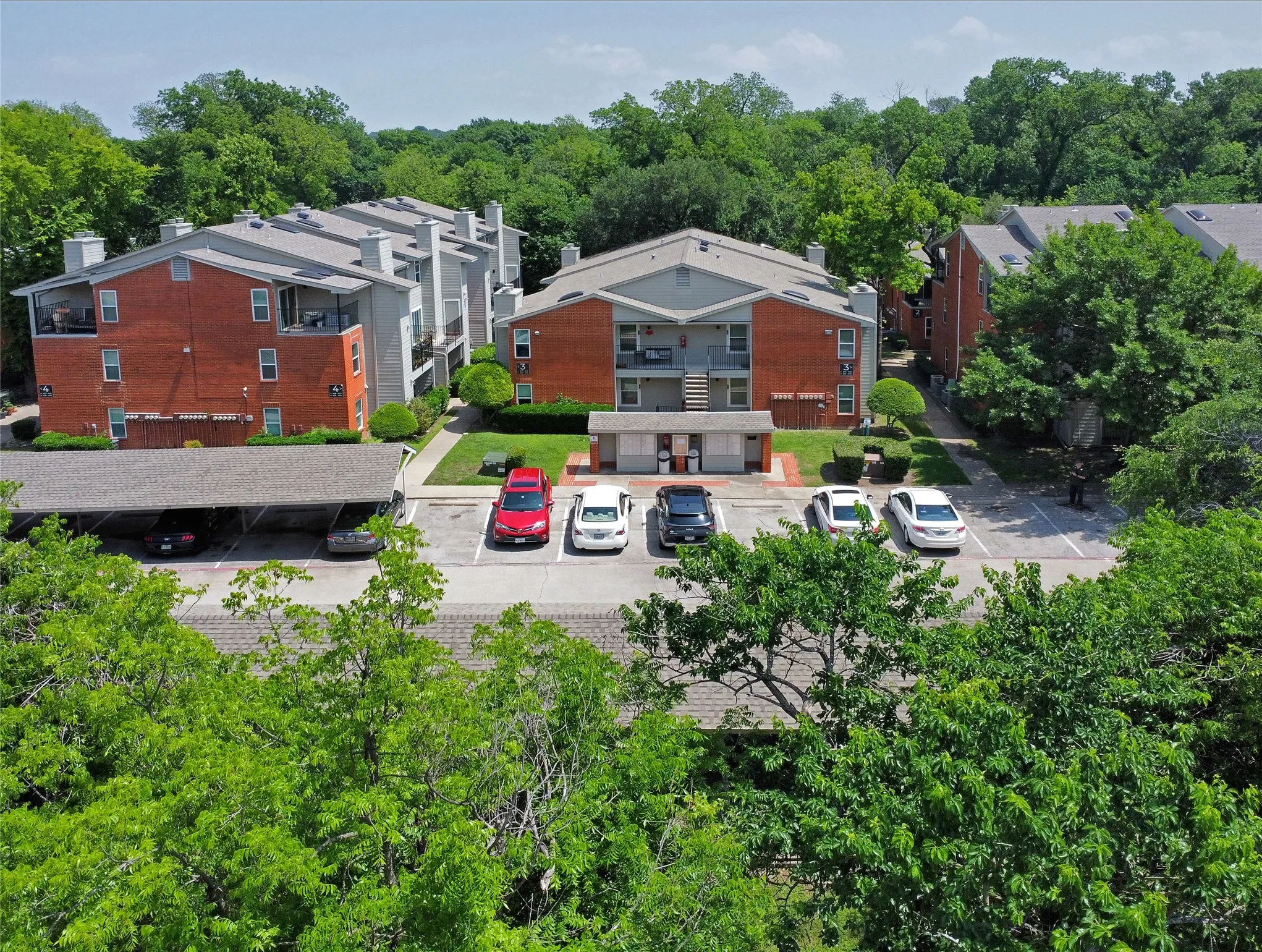 Bird's-eye drone photo of exterior front view of property, community mailboxes and designated covered parking in the gated community.