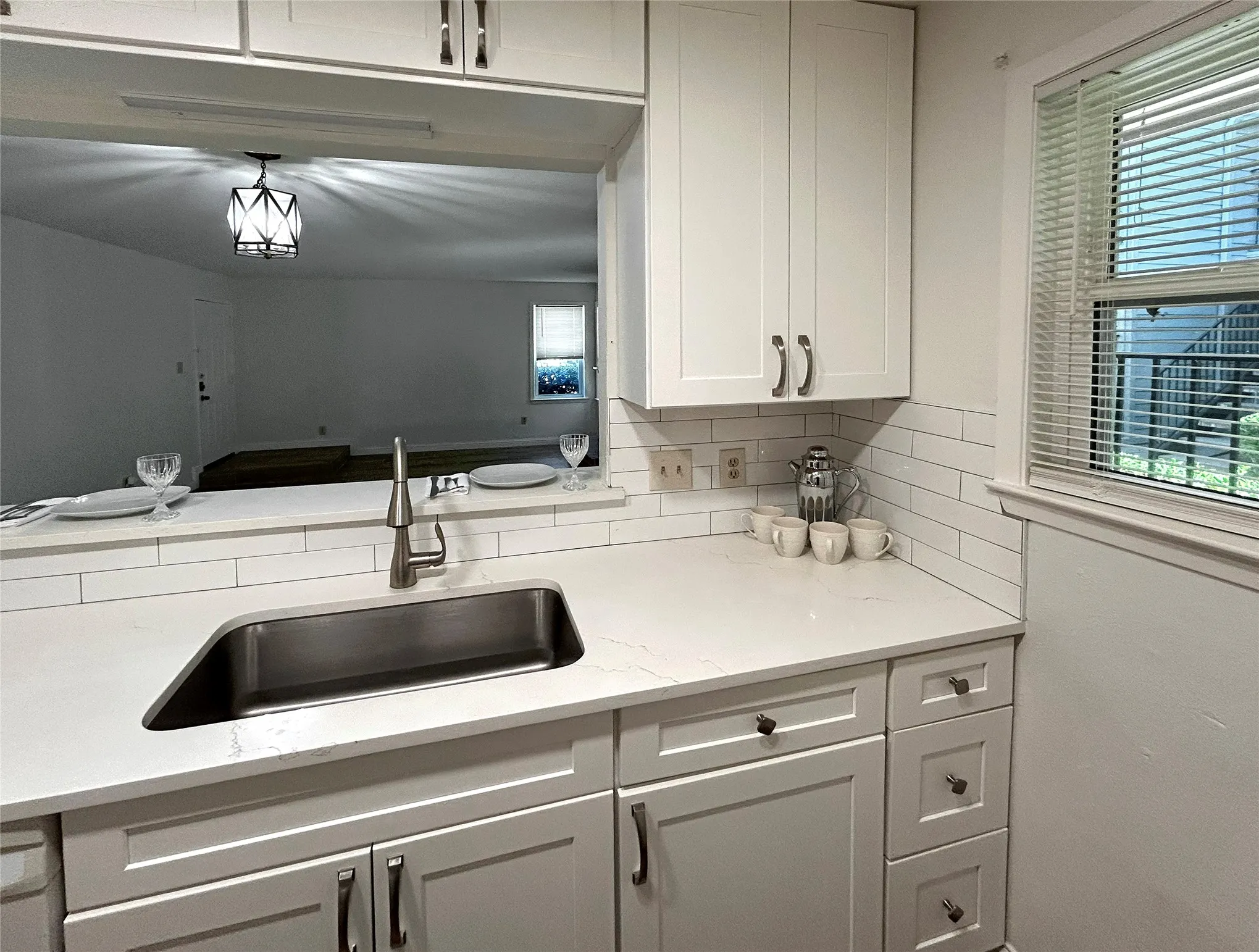 The kitchen has a window, breakfast bar, stainless steel sink, white dishwasher, white cabinetry, designer cabinets and subway tile backsplash.