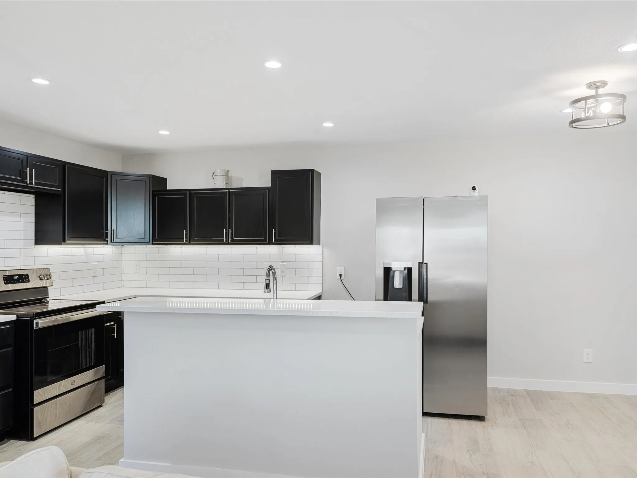 Kitchen with dark cabinets, a kitchen island, stainless steel appliances, decorative backsplash, and recessed lighting