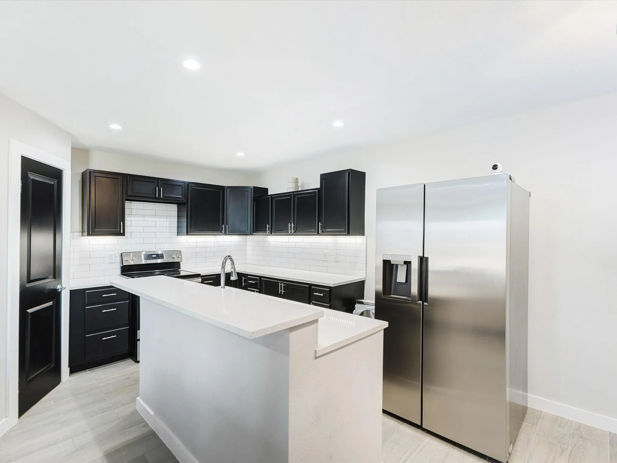 Kitchen featuring dark cabinetry, stainless steel appliances, a kitchen island with sink, light stone countertops, and recessed lighting