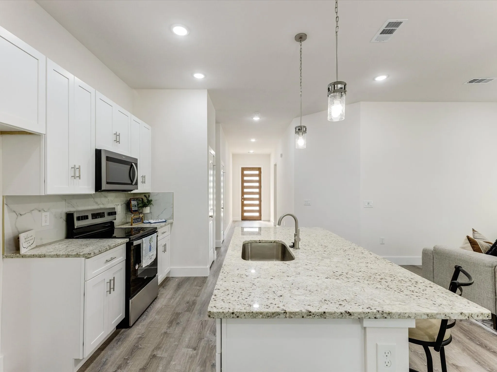 Kitchen with stainless steel appliances, a center island with sink, a breakfast bar area, white cabinets, and light stone counters