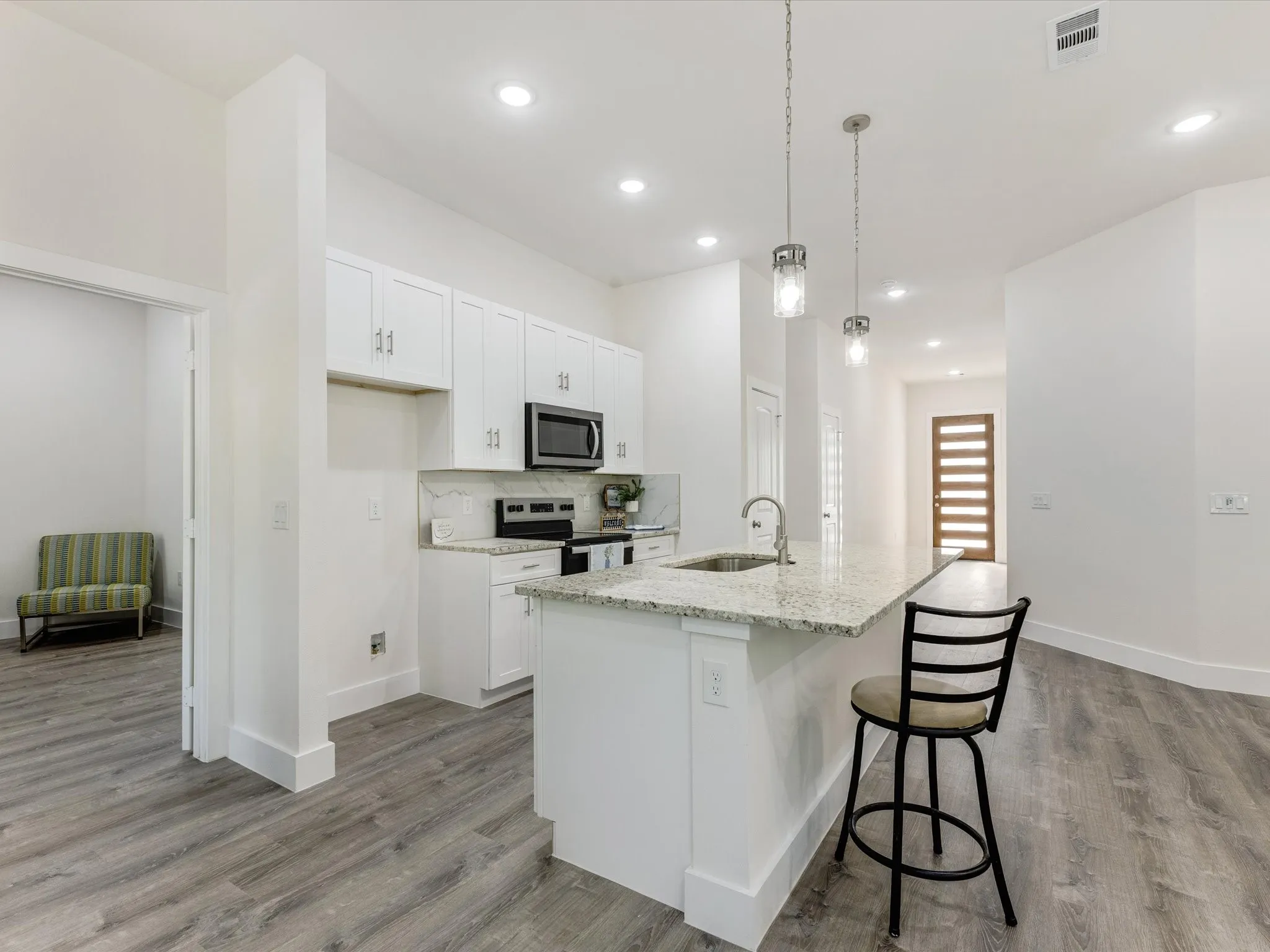 Kitchen featuring white cabinets, a breakfast bar, stainless steel appliances, light stone counters, and hanging light fixtures