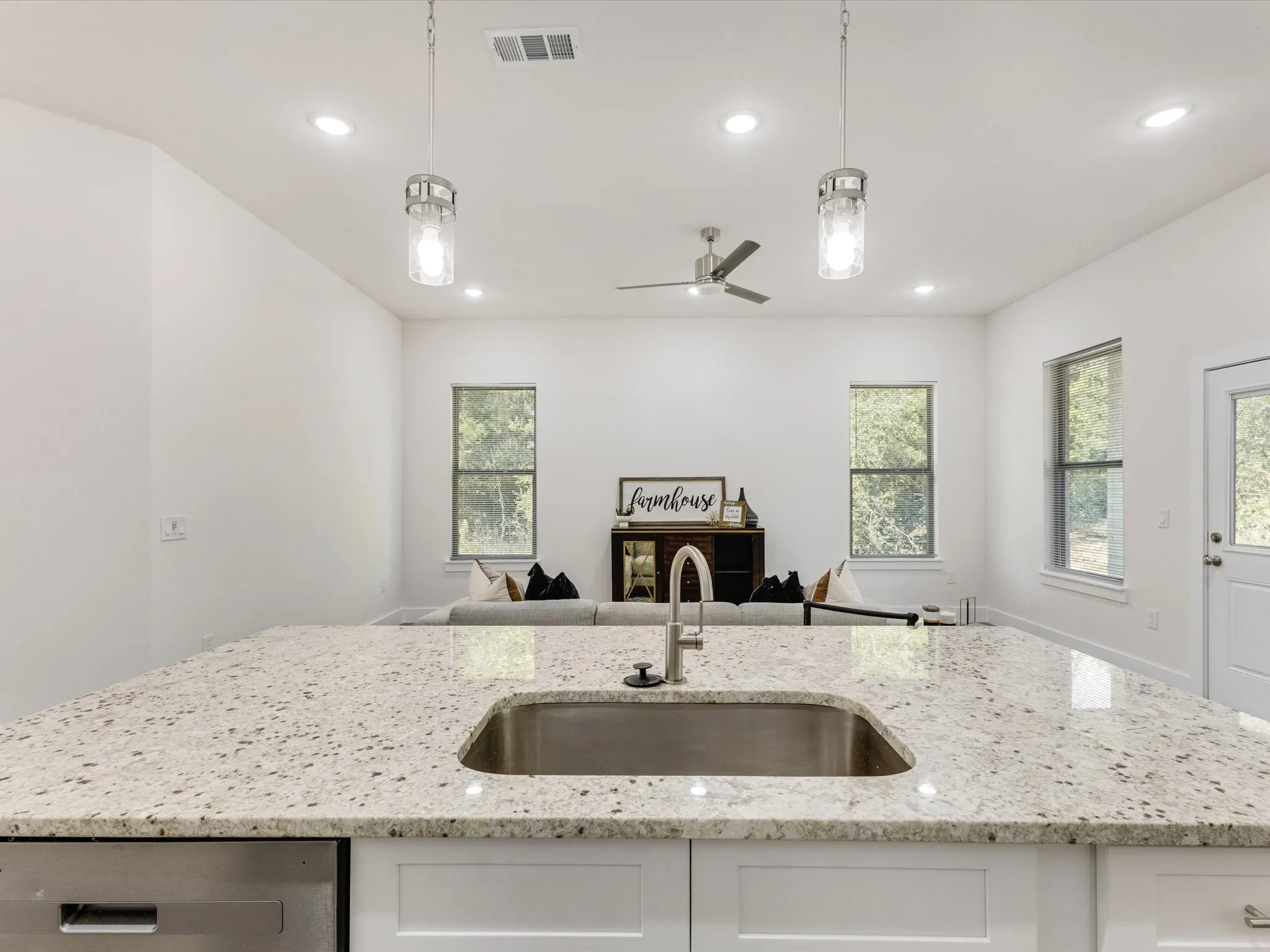 Kitchen featuring hanging light fixtures, light stone countertops, a center island with sink, a ceiling fan, and white cabinets