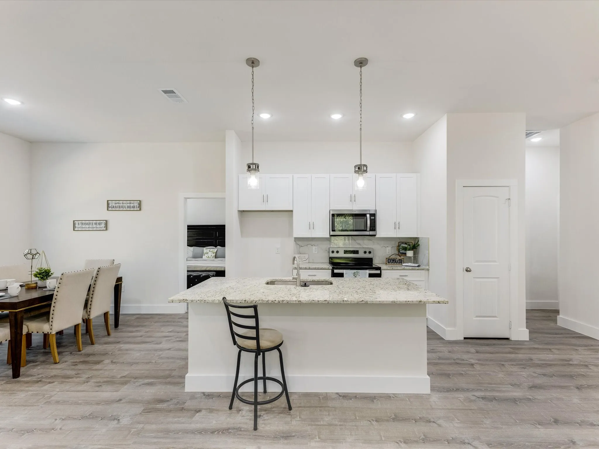 Kitchen with decorative light fixtures, stainless steel appliances, white cabinetry, light wood finished floors, and light stone countertops