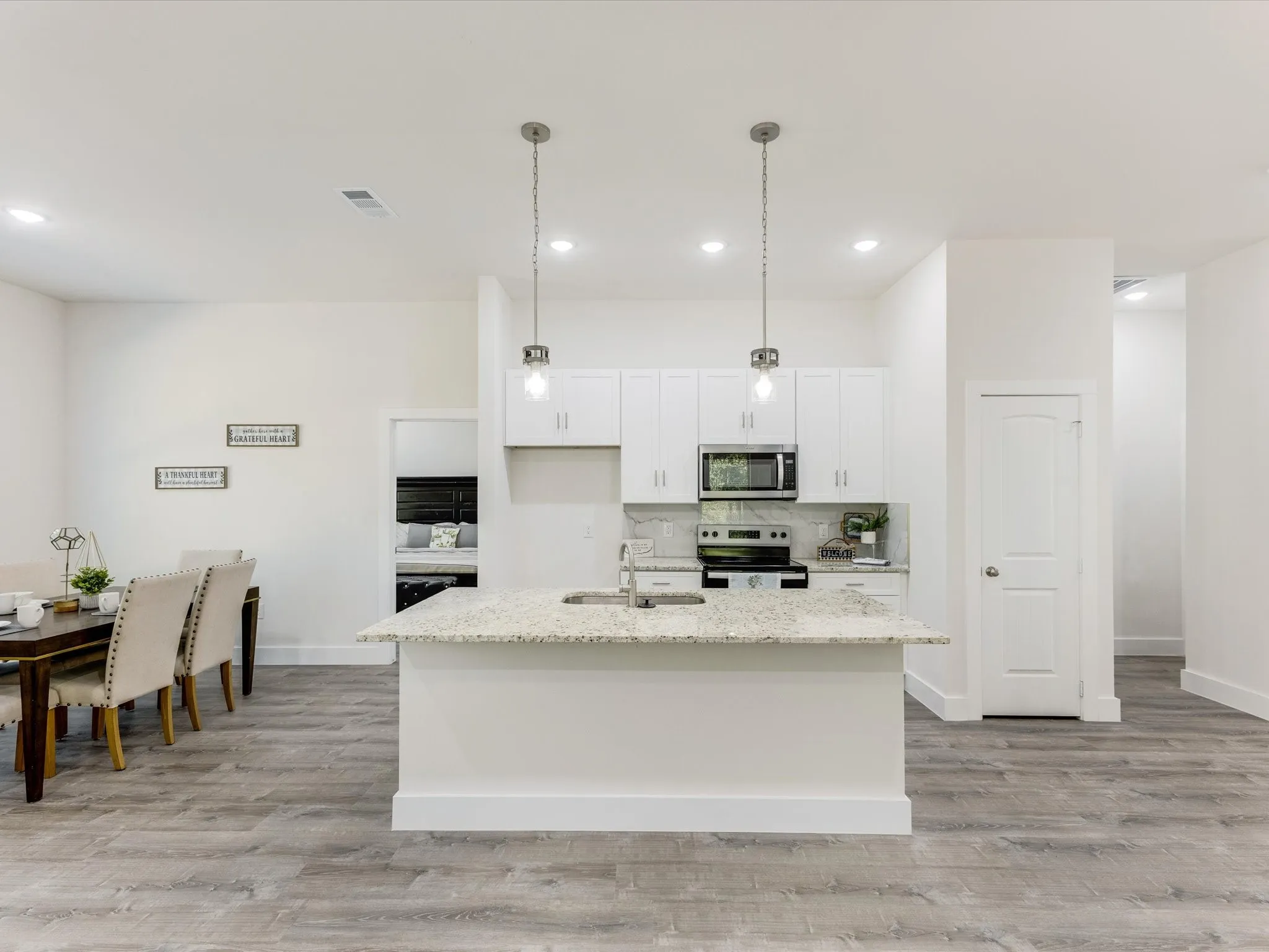 Kitchen featuring stainless steel appliances, an island with sink, hanging light fixtures, white cabinetry, and light stone countertops