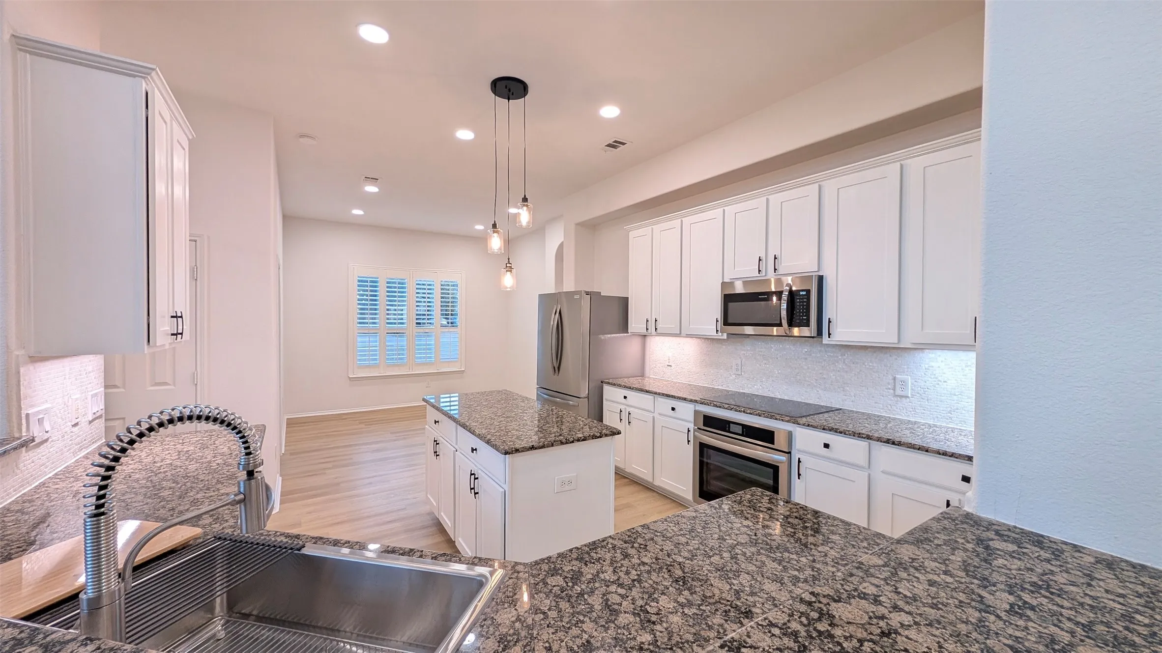 Kitchen with white cabinets, dark stone counters, backsplash, decorative light fixtures, and a center island