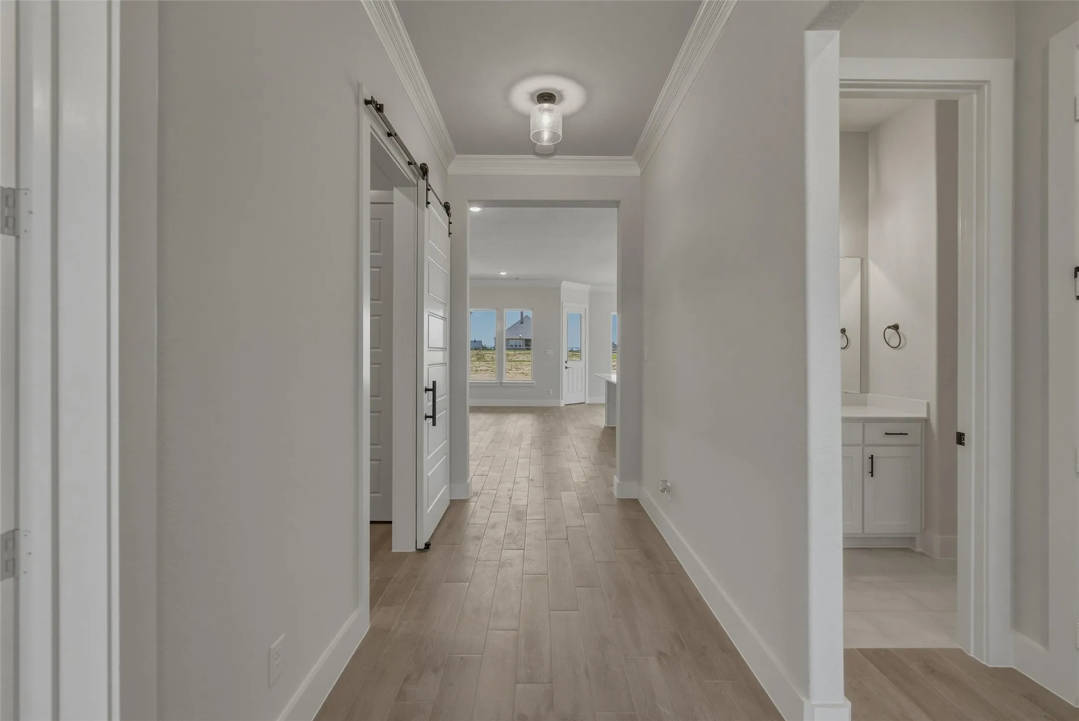 Hallway featuring wood-finish flooring, crown molding, and a visible barn door
