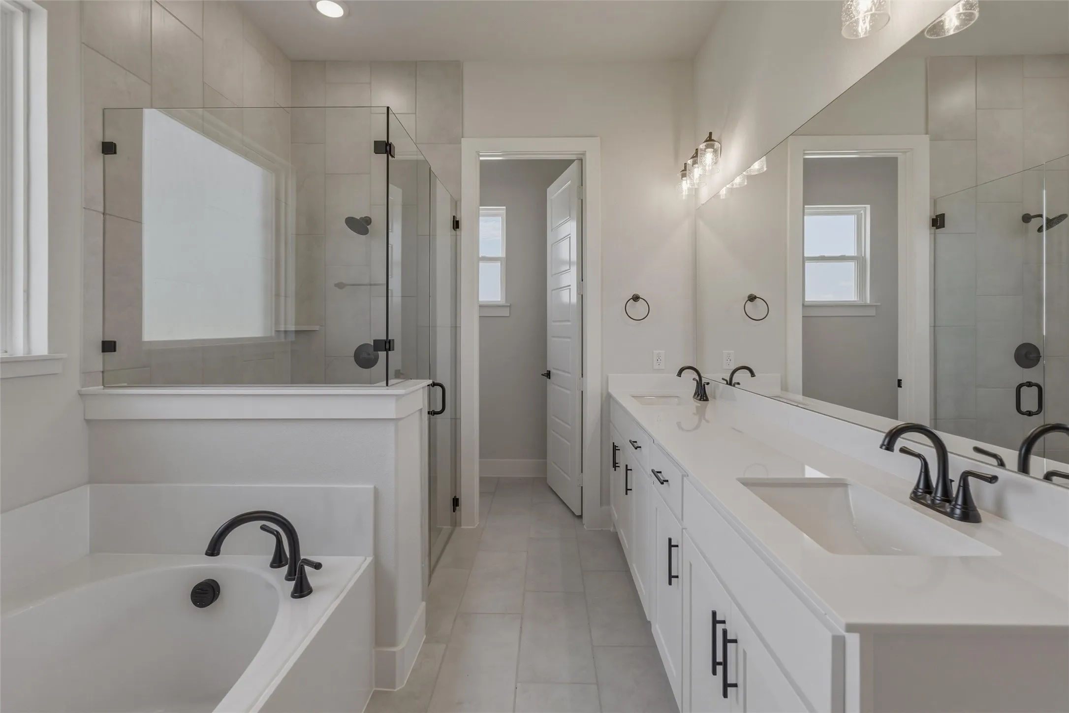 Modern bathroom featuring a dual vanity with white cabinetry and integrated sinks, a freestanding tub, and a frameless glass shower with matte black fixtures