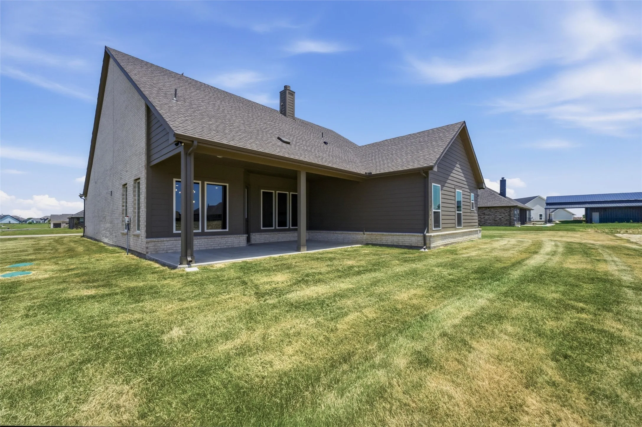 Rear exterior featuring an expansive concrete patio, covered porch area with support columns, and multiple windows