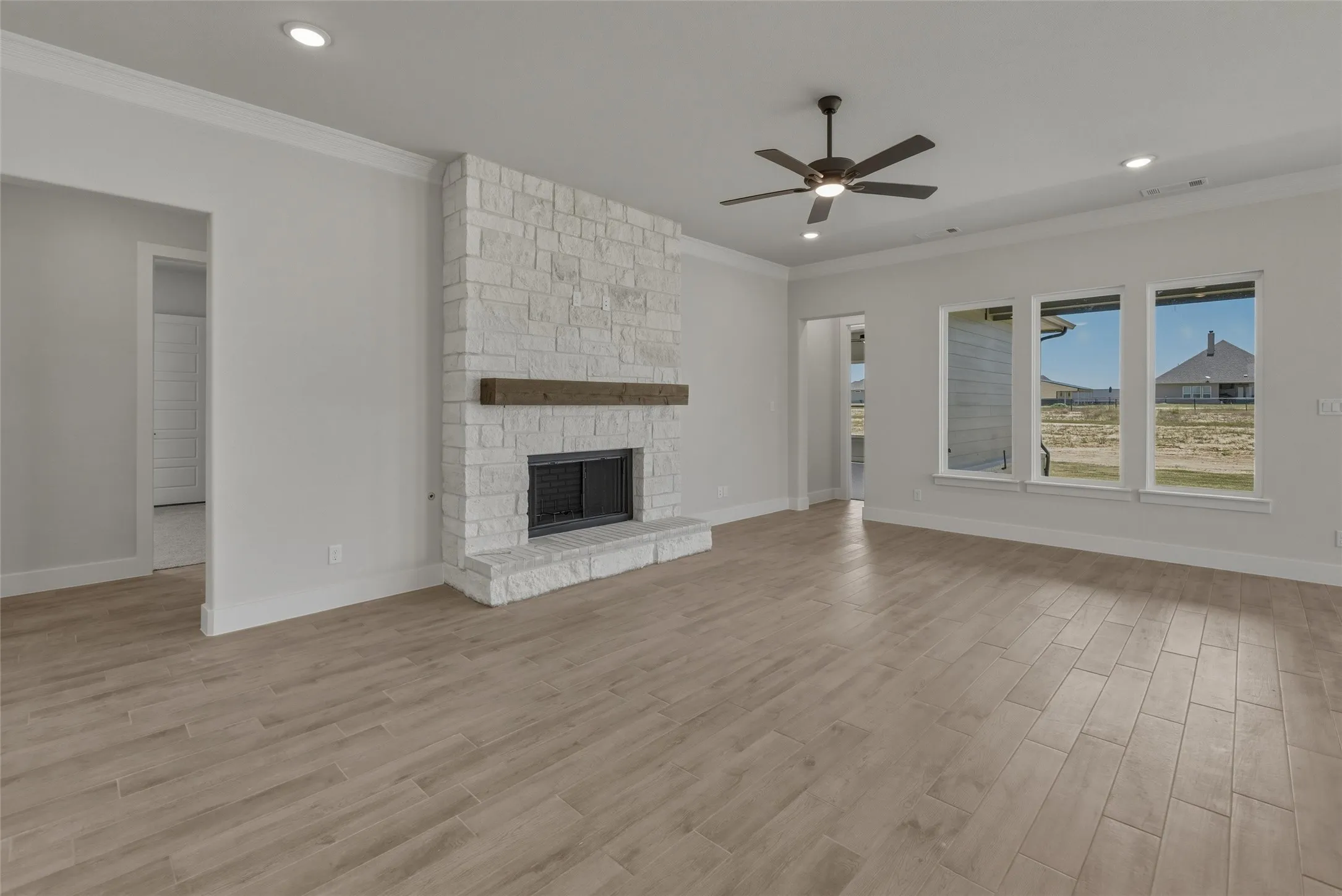 Living space featuring a stone fireplace with a wood-finish mantel, wood-finish flooring, recessed lighting, and multiple windows