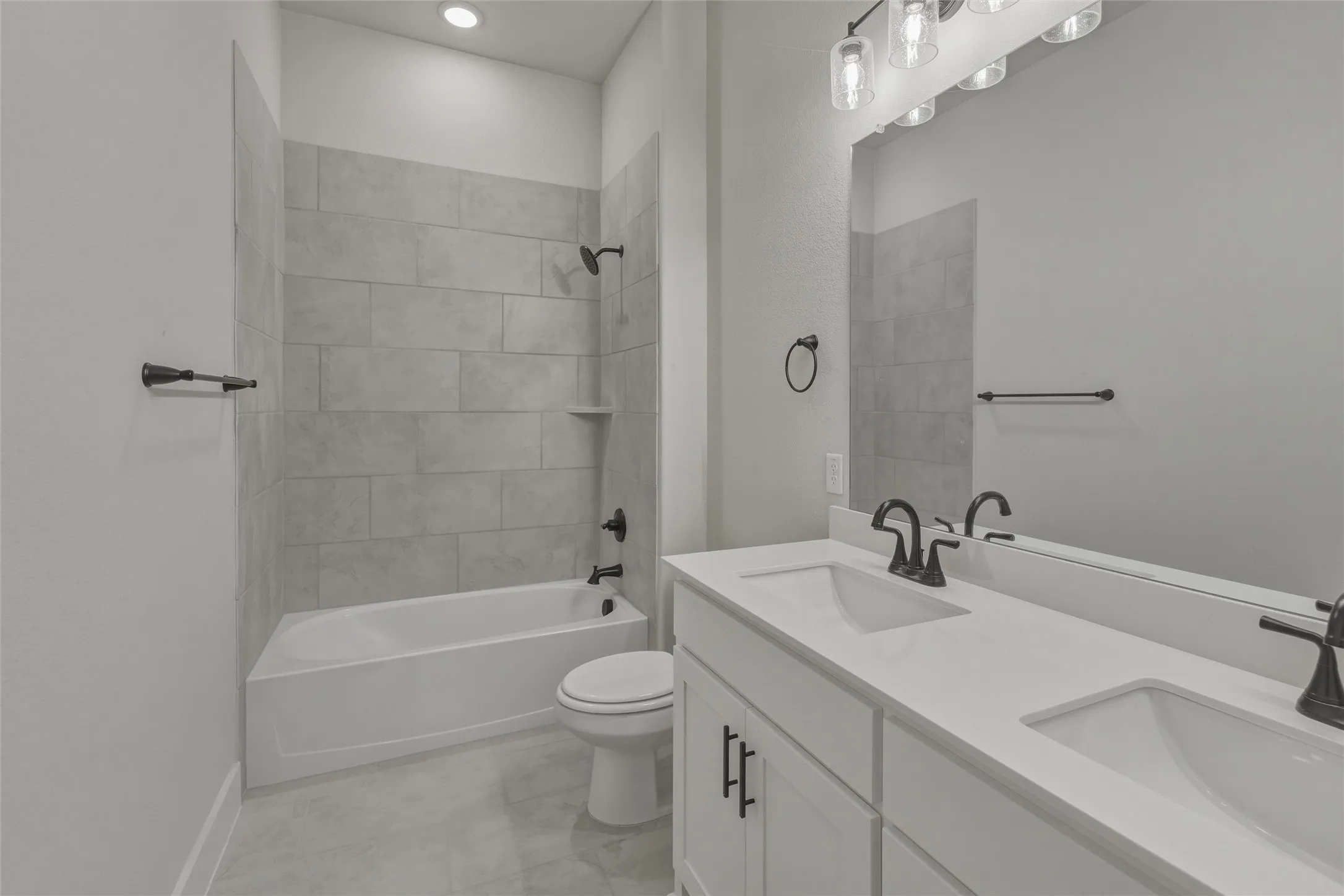 Bathroom with a dual vanity featuring white countertops and cabinetry, matte black fixtures, and a large wall-mounted mirror