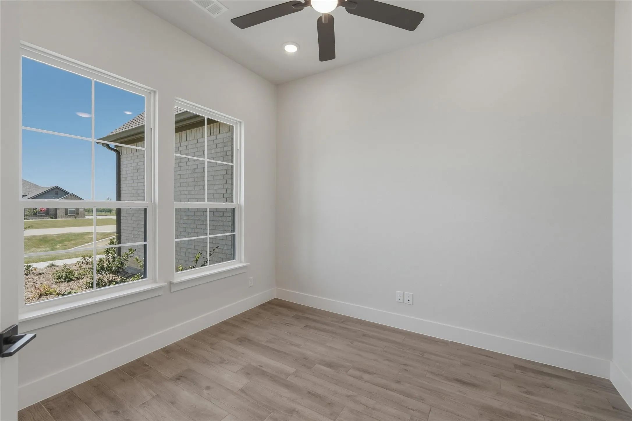 Light-filled room featuring two multi-pane windows, wood-finish flooring, a ceiling fan with integrated lighting, and recessed ceiling lights