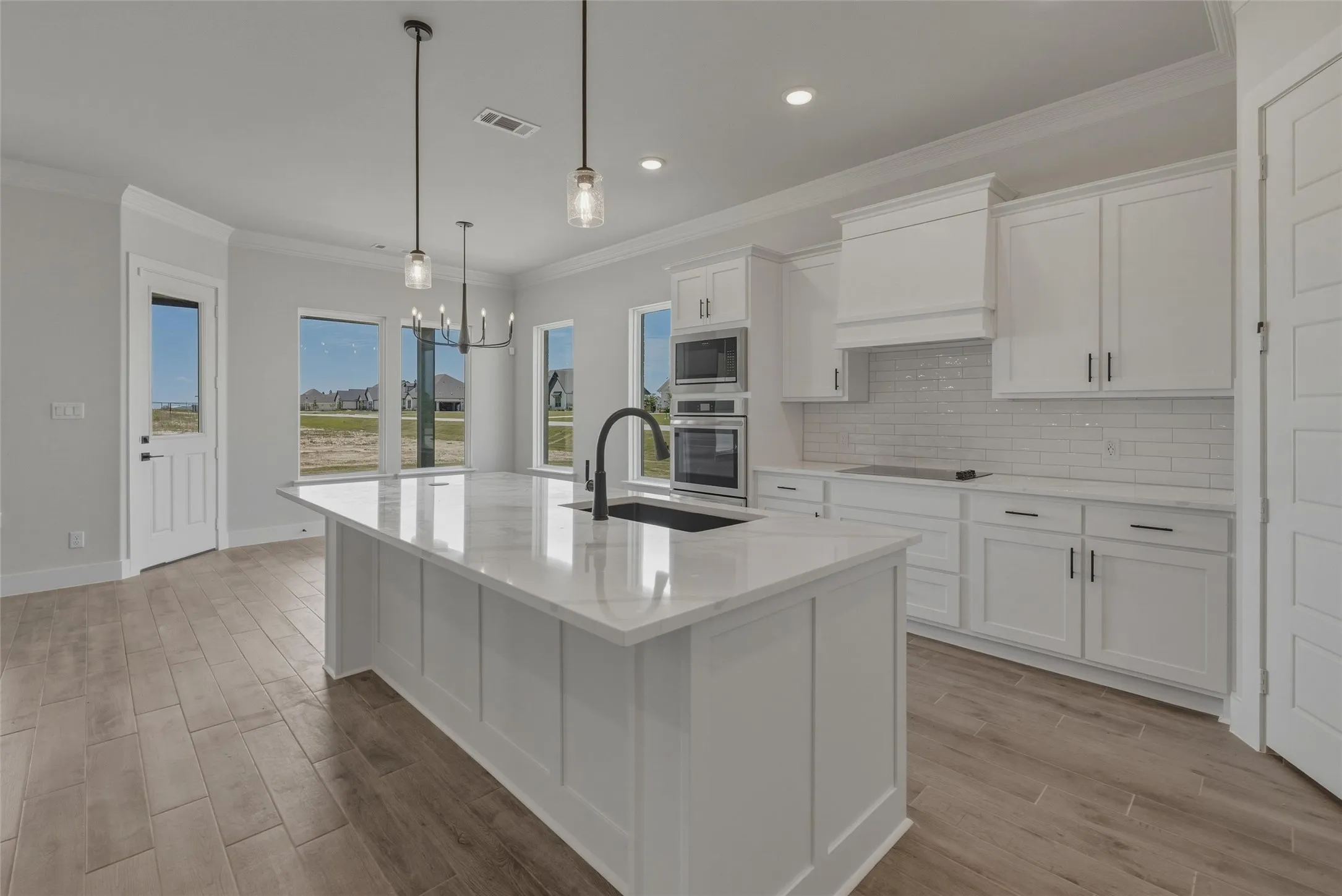 Modern kitchen featuring an expansive center island with a white countertop and integrated sink, white shaker cabinetry, stainless steel built-in appliances, and wood-finish flooring