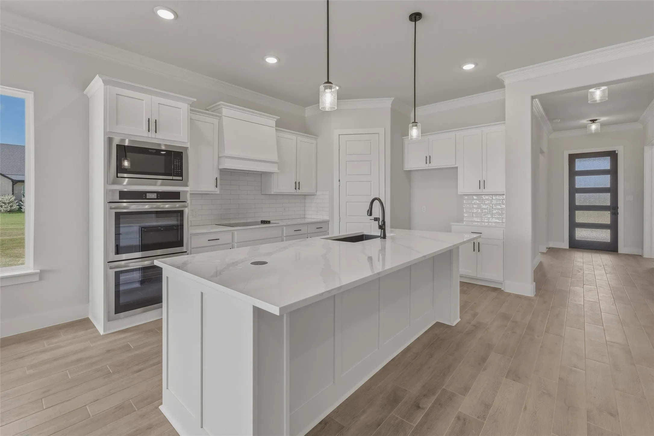Kitchen featuring a large central island with a sink, white cabinetry, integrated stainless steel appliances, and wood-finish flooring
