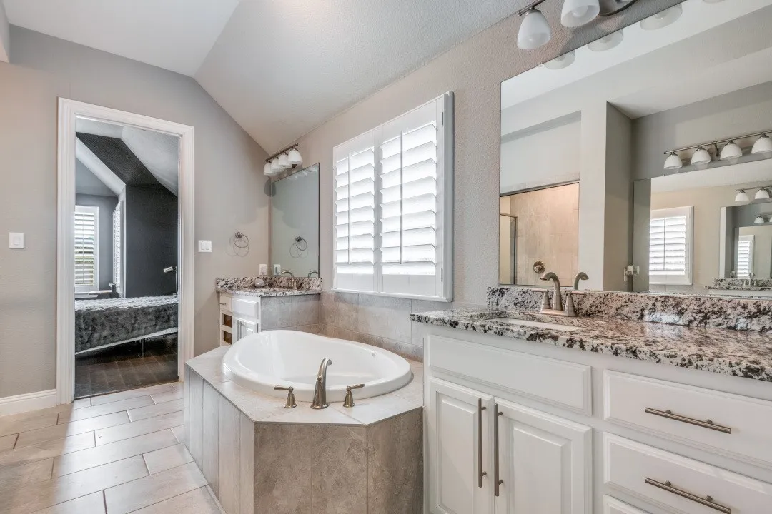 Full bathroom with a bath, two vanities, lofted ceiling, and light tile patterned floors