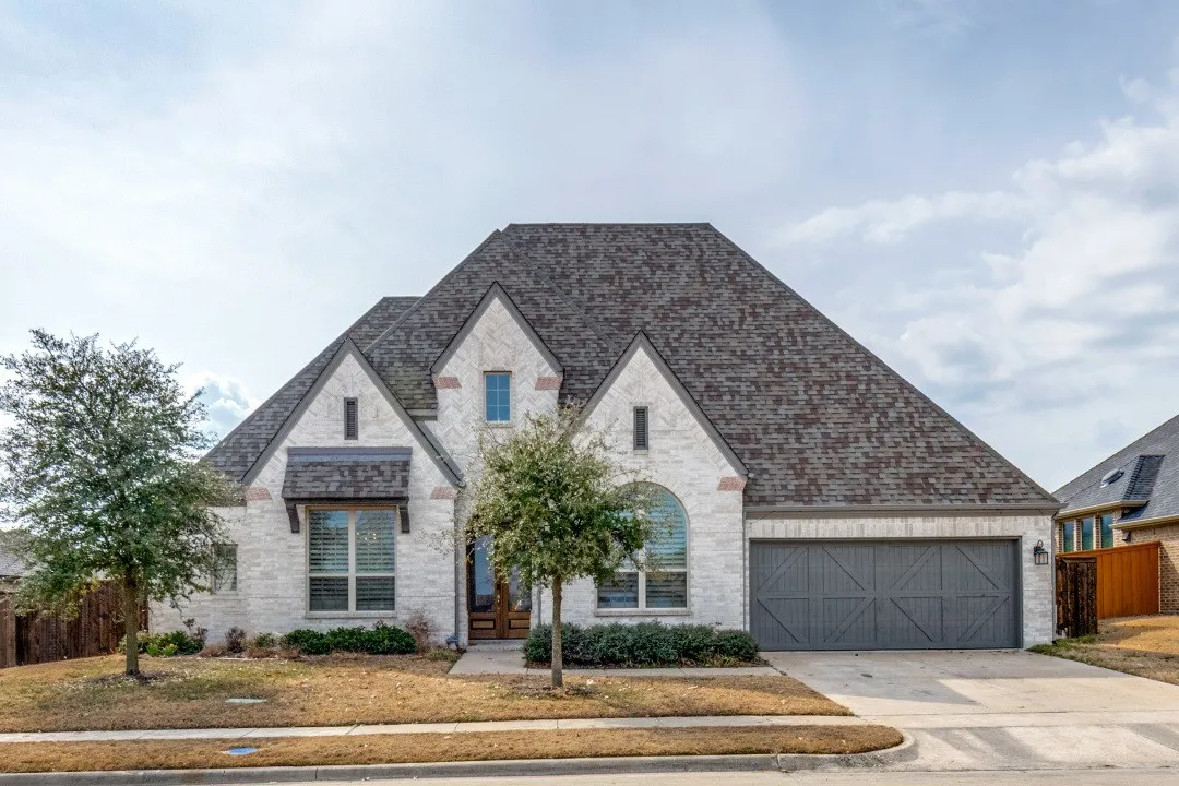 French country home featuring brick siding, driveway, stone siding, roof with shingles, and a garage