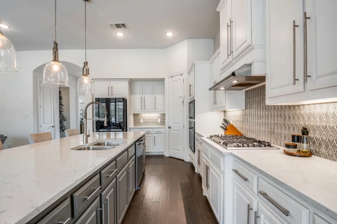 Kitchen featuring light stone countertops, tasteful backsplash, two tone cabinets, pendant lighting, and dark wood-type flooring