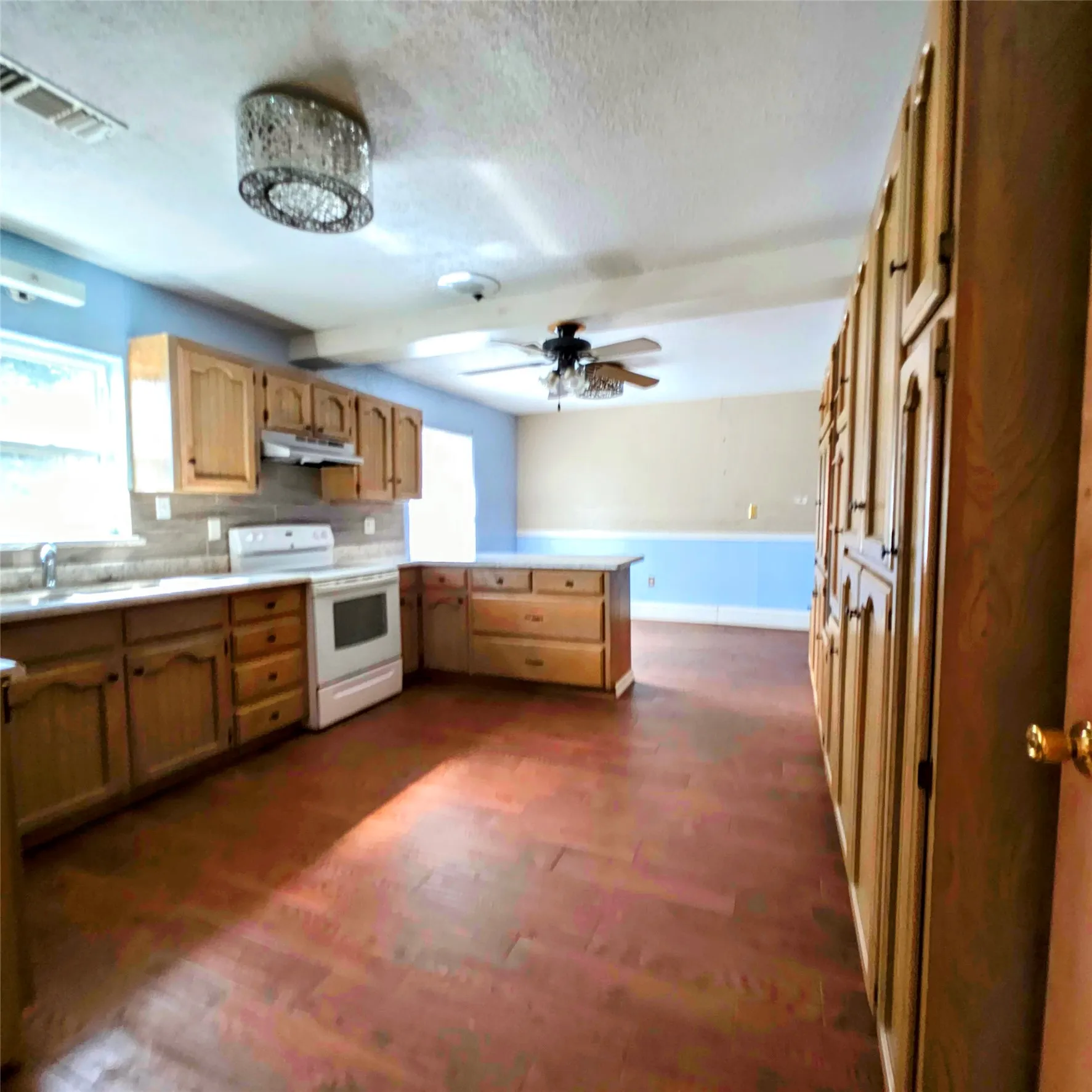 Kitchen featuring white electric range oven, light countertops, a peninsula, dark wood-style floors, and tasteful backsplash