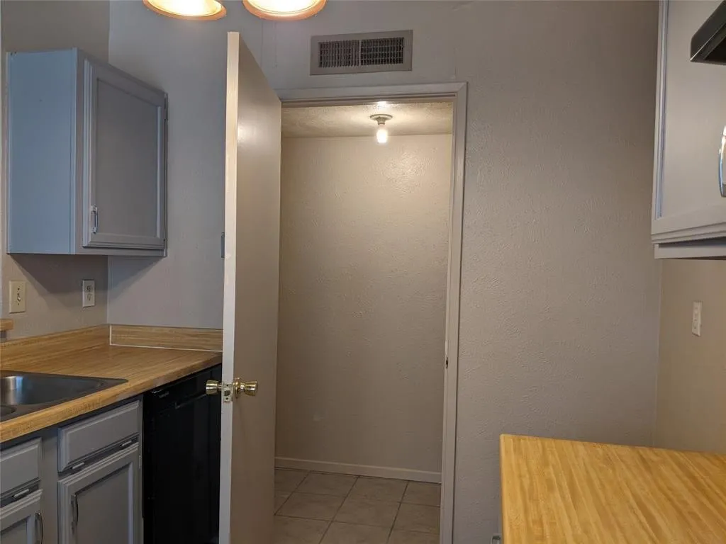 Kitchen featuring light countertops, gray cabinets, dishwasher, light tile patterned flooring, and ventilation hood