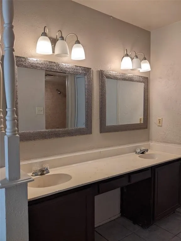 Full bath featuring double vanity, a textured wall, tile patterned floors, and a tile shower