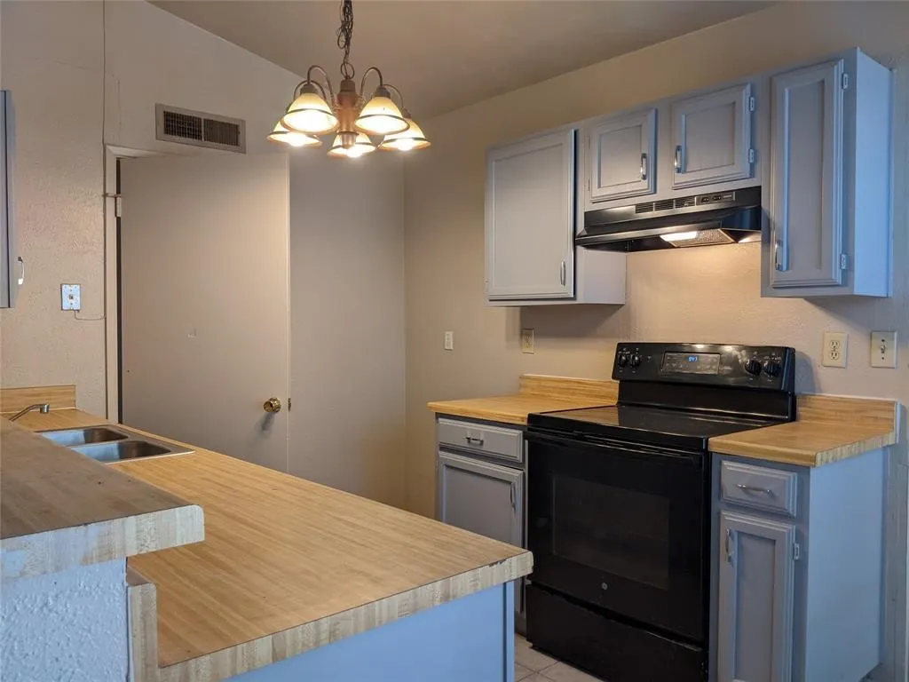 Kitchen featuring black electric range oven, light countertops, lofted ceiling, and a chandelier