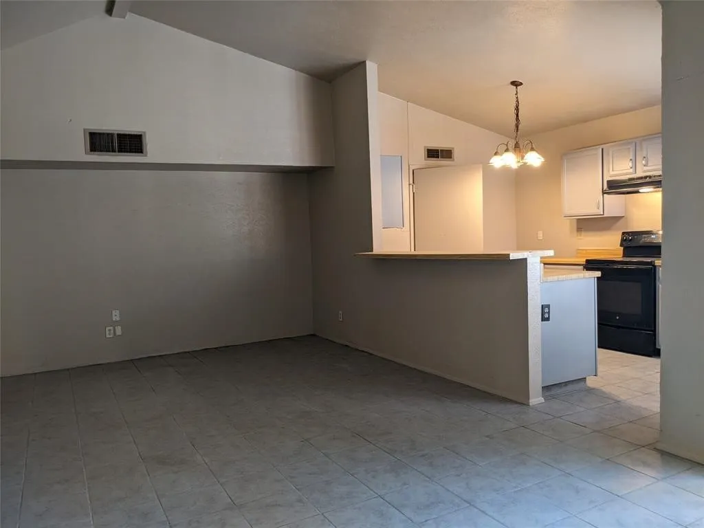 Kitchen featuring light countertops, black range with electric cooktop, hanging lights, a peninsula, and white cabinets