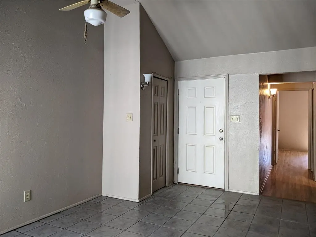 Entrance foyer with a textured wall, ceiling fan, dark tile patterned flooring, and lofted ceiling