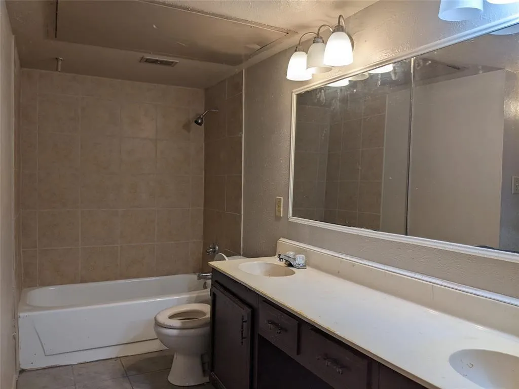 Bathroom with double vanity, bathtub / shower combination, a textured wall, and tile patterned floors