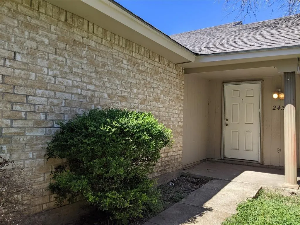 Doorway to property featuring brick siding and roof with shingles