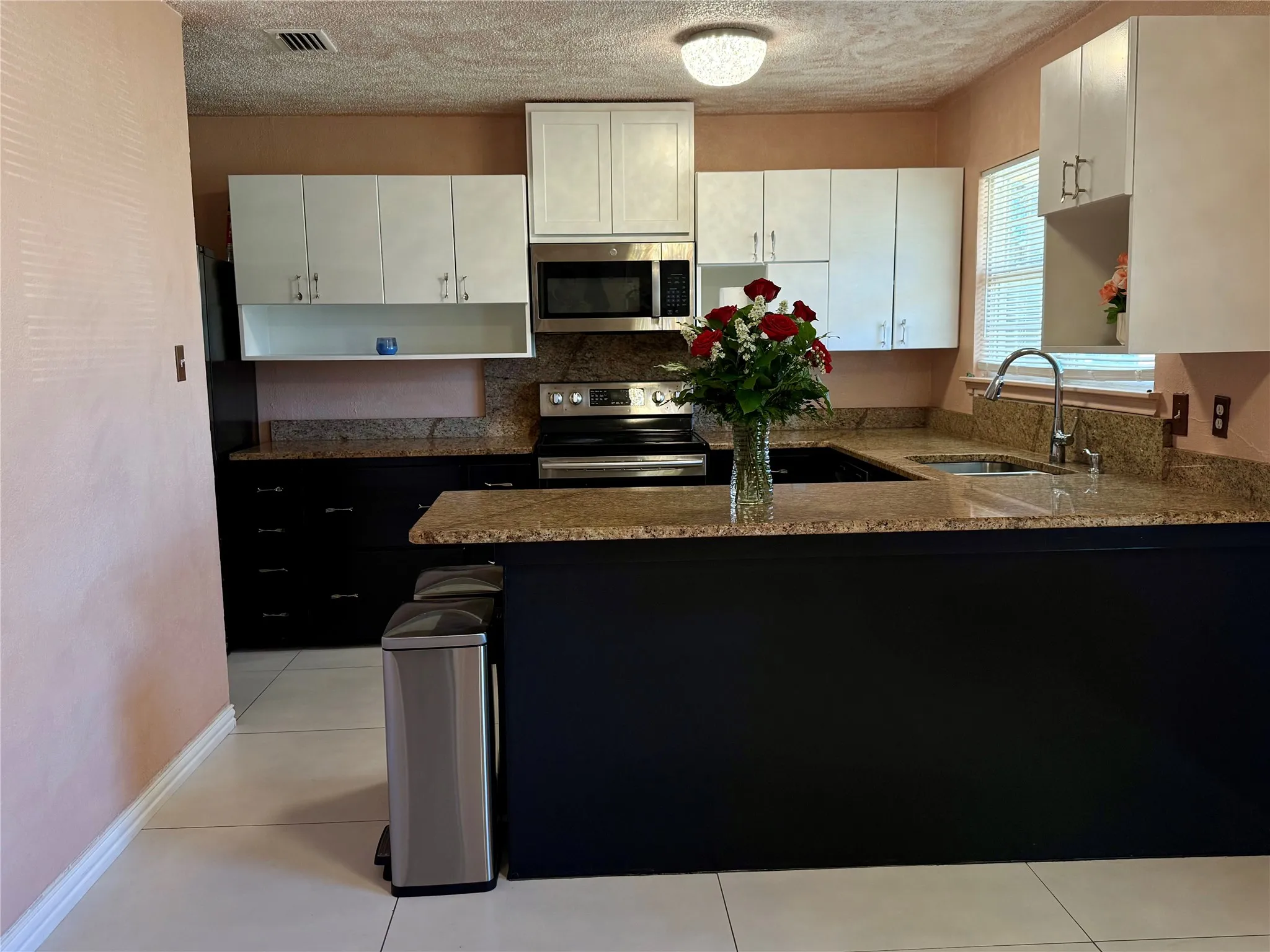 Two tone kitchen with a peninsula, light stone countertops, stainless steel appliances, light tile patterned floors, and a textured ceiling