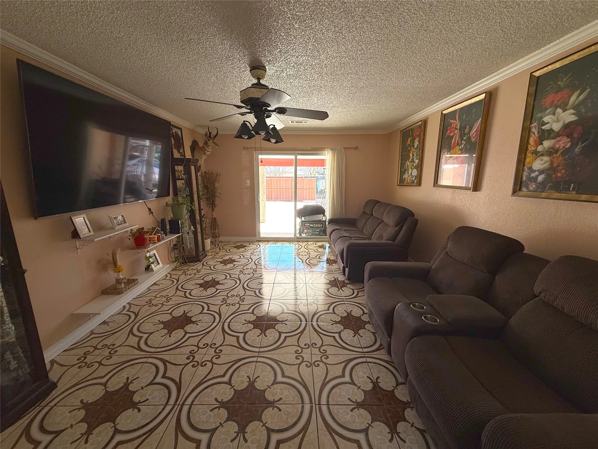 Tiled living area with ornamental molding, ceiling fan, and a textured ceiling