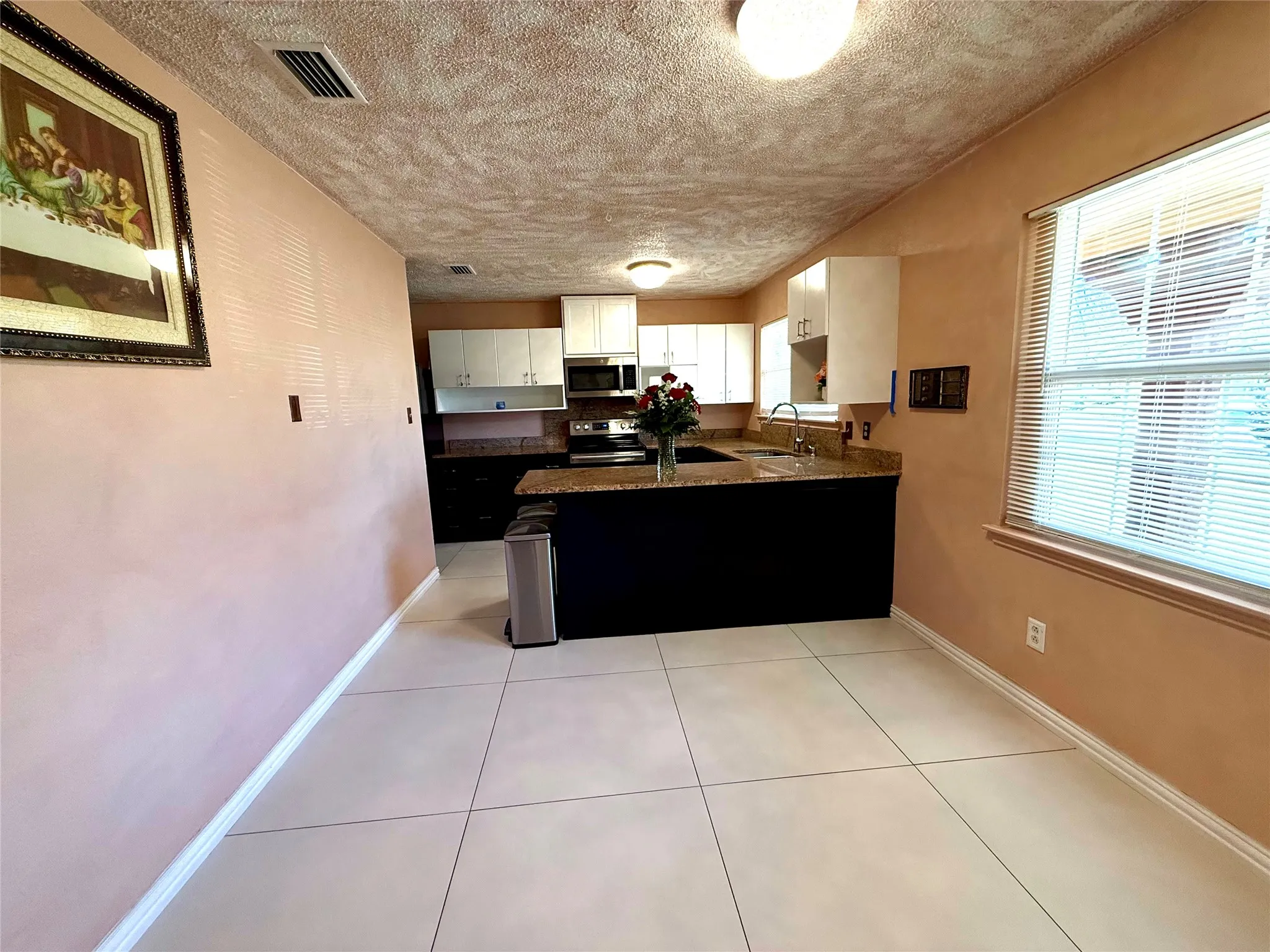 Kitchen with light tile patterned floors, a peninsula, a textured ceiling, stainless steel appliances, and dark stone counters