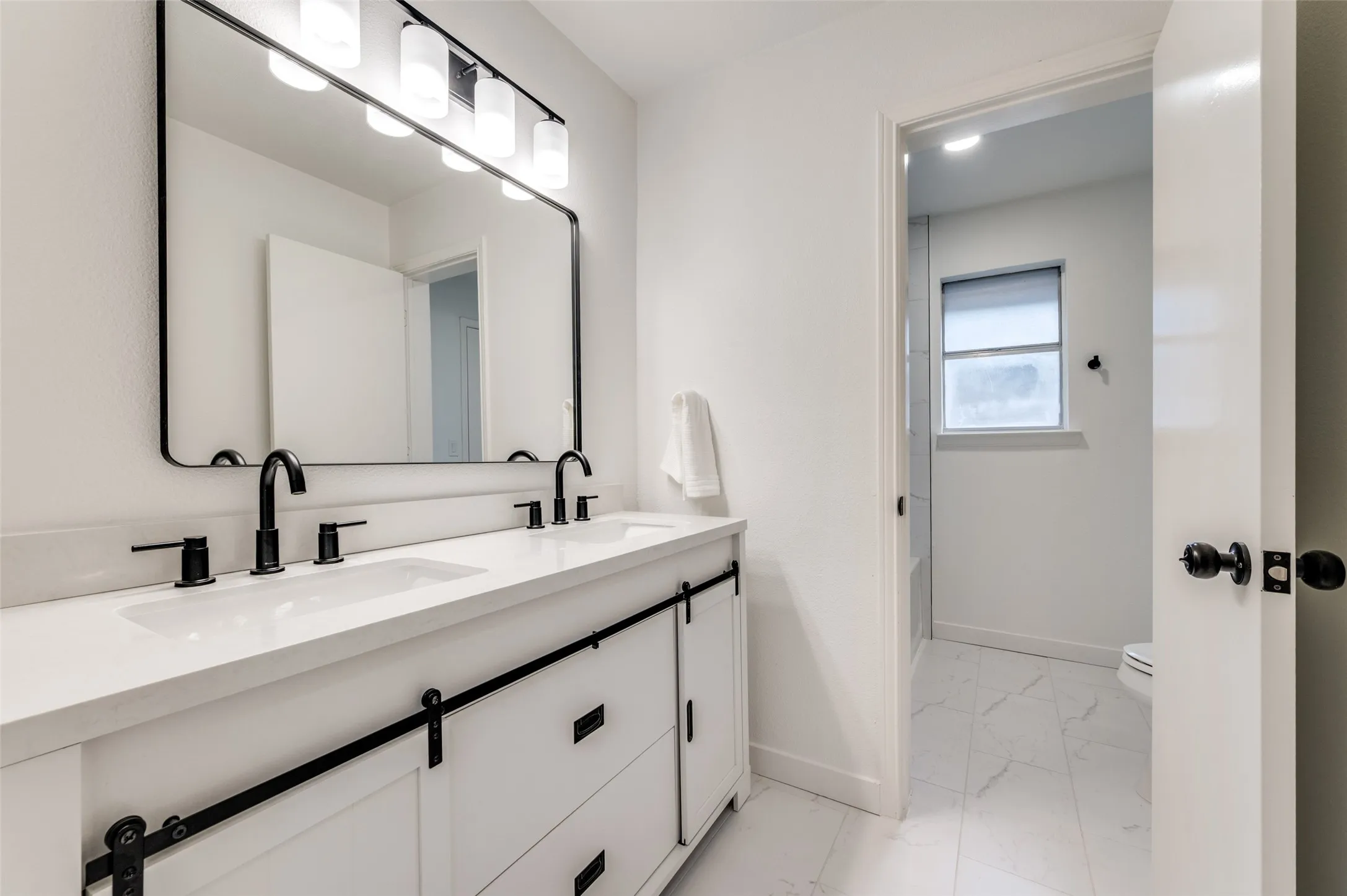 Updated guest bathroom with dual sink vanity, modern black fixtures, framed mirror, and upgraded lighting.
