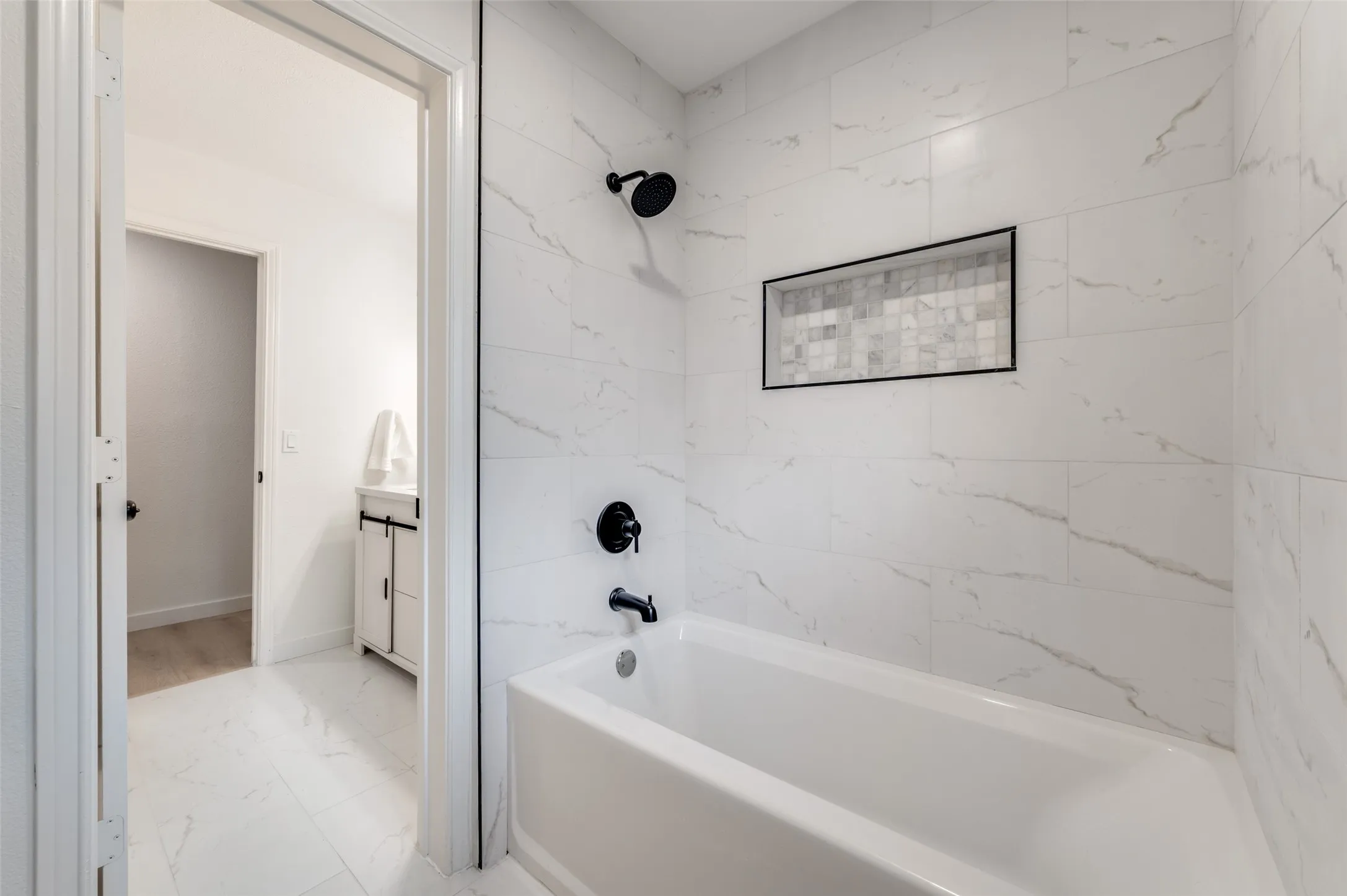 Tub / shower combo finished with porcelain tile, marble accent niche, and sleek black hardware.
