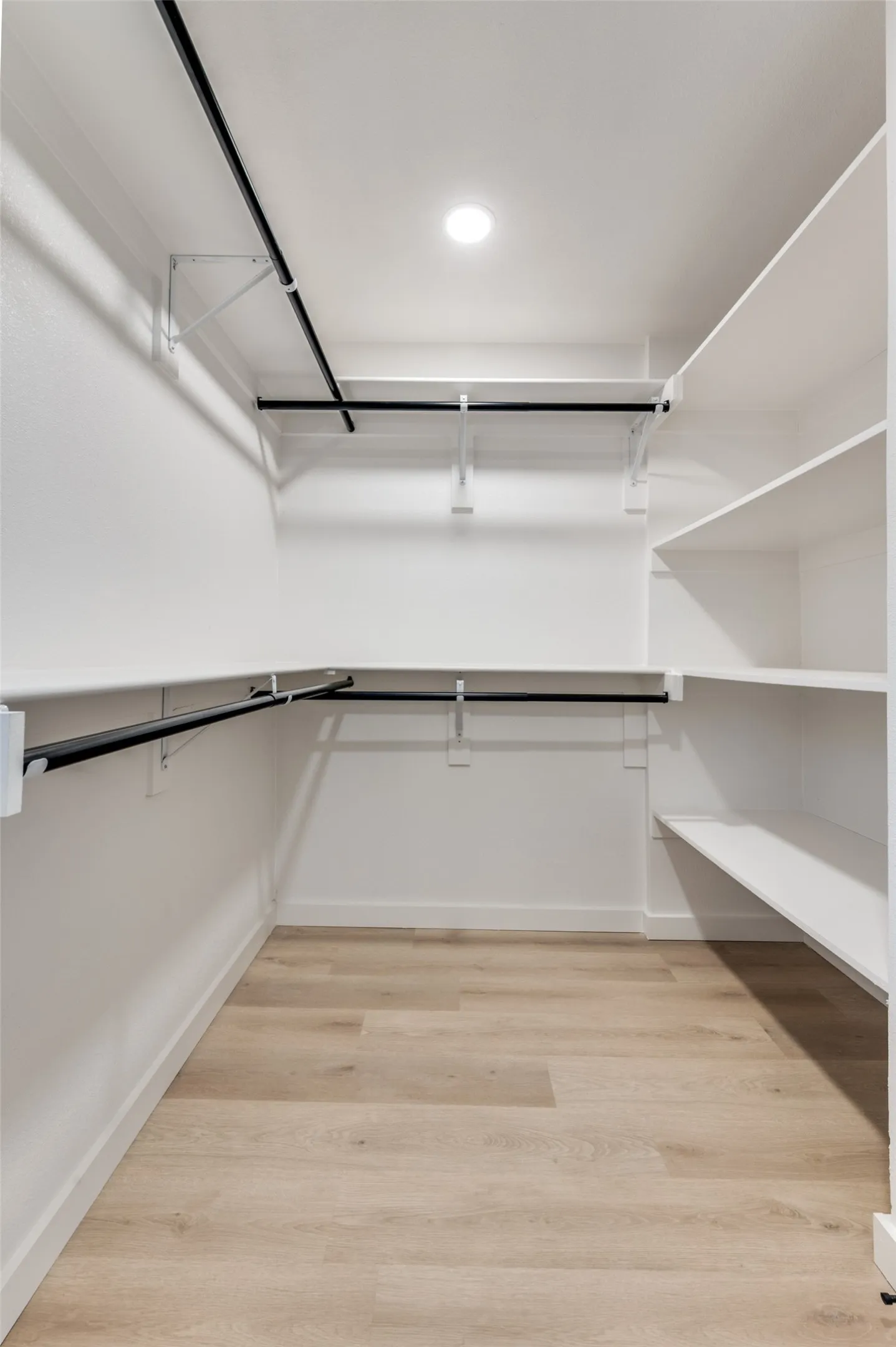 Spacious walk-in closet featuring custom shelving, double hanging rods, and upgraded lighting for excellent storage and organization.