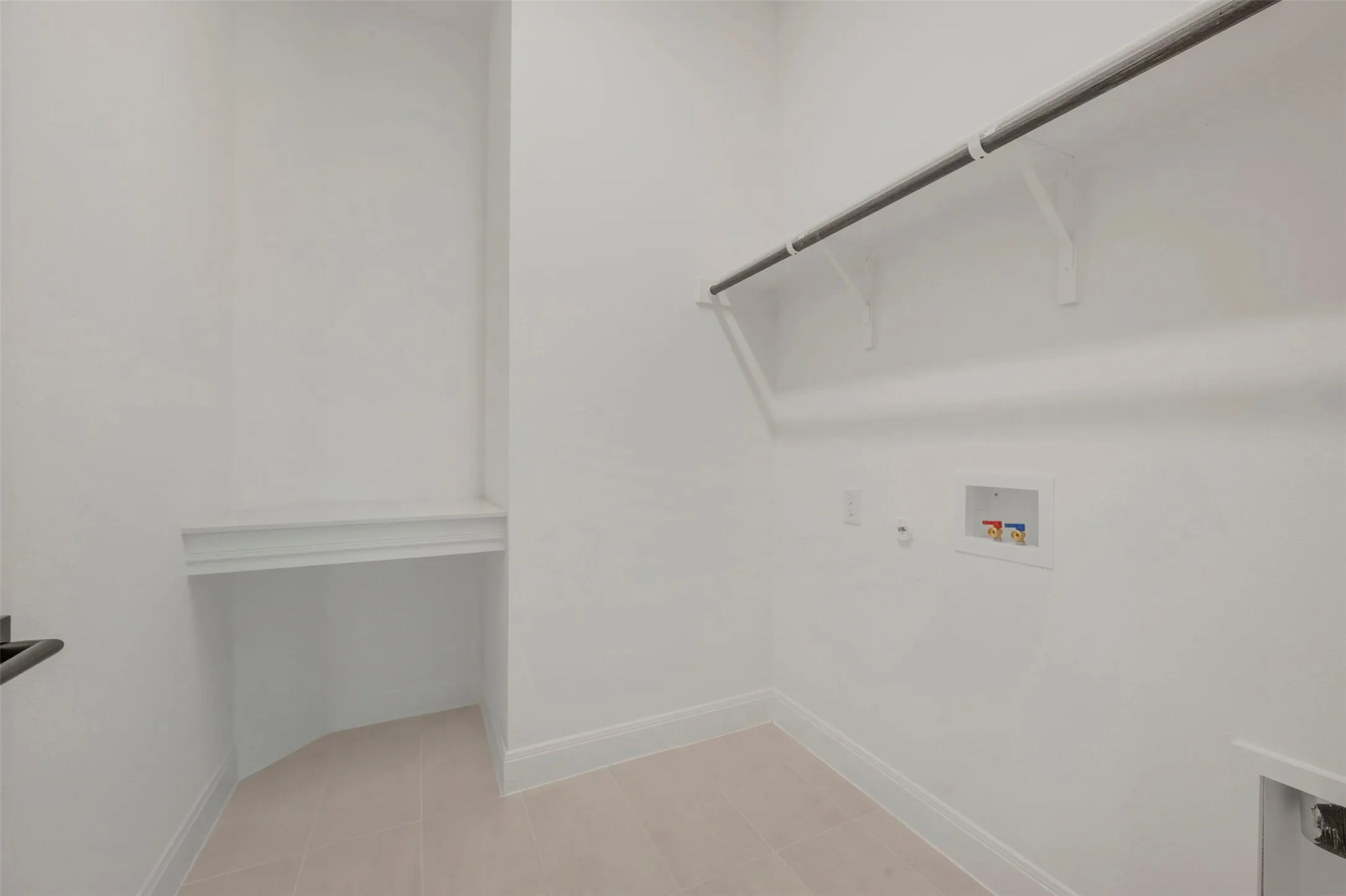 Dedicated laundry area featuring a built-in hanging rod, wall-mounted shelf supports, washer/dryer hookups, and light-colored tile flooring