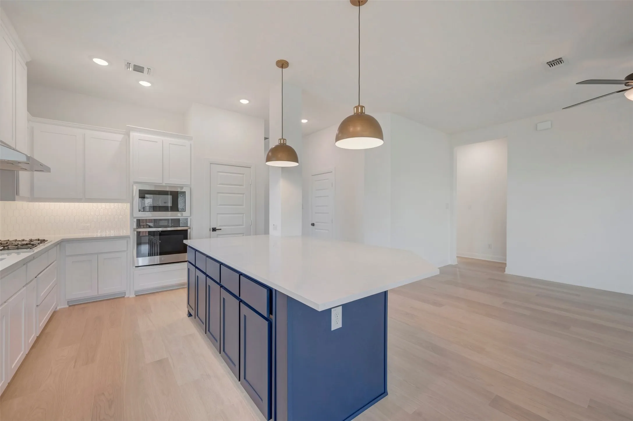 Contemporary kitchen featuring a large central island with a solid surface countertop and navy cabinetry, light wood-finish flooring, white upper and lower perimeter cabinetry, stainless steel appliances, and a white geometric tile backsplash